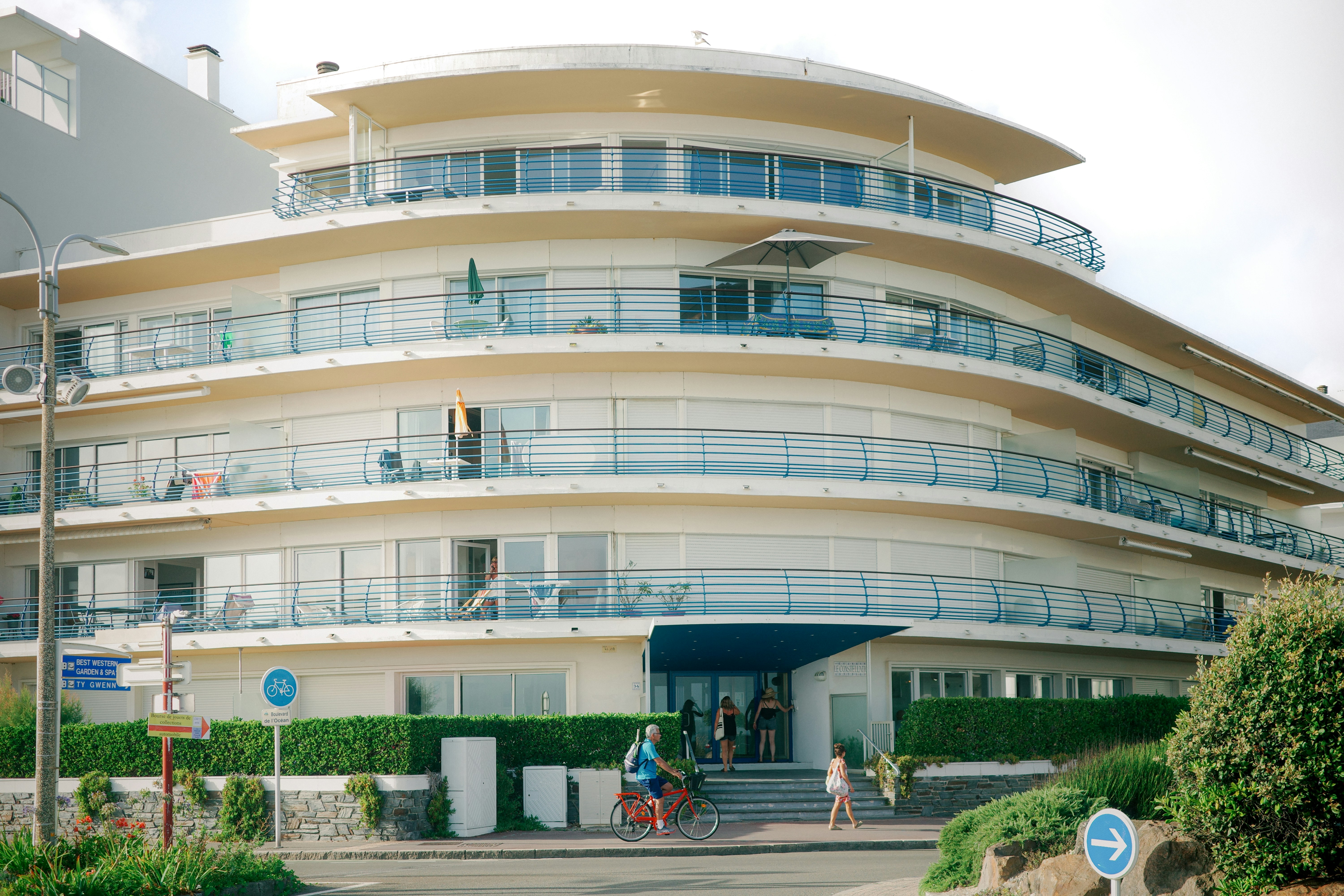 Modern curved building with balconies and people entering.