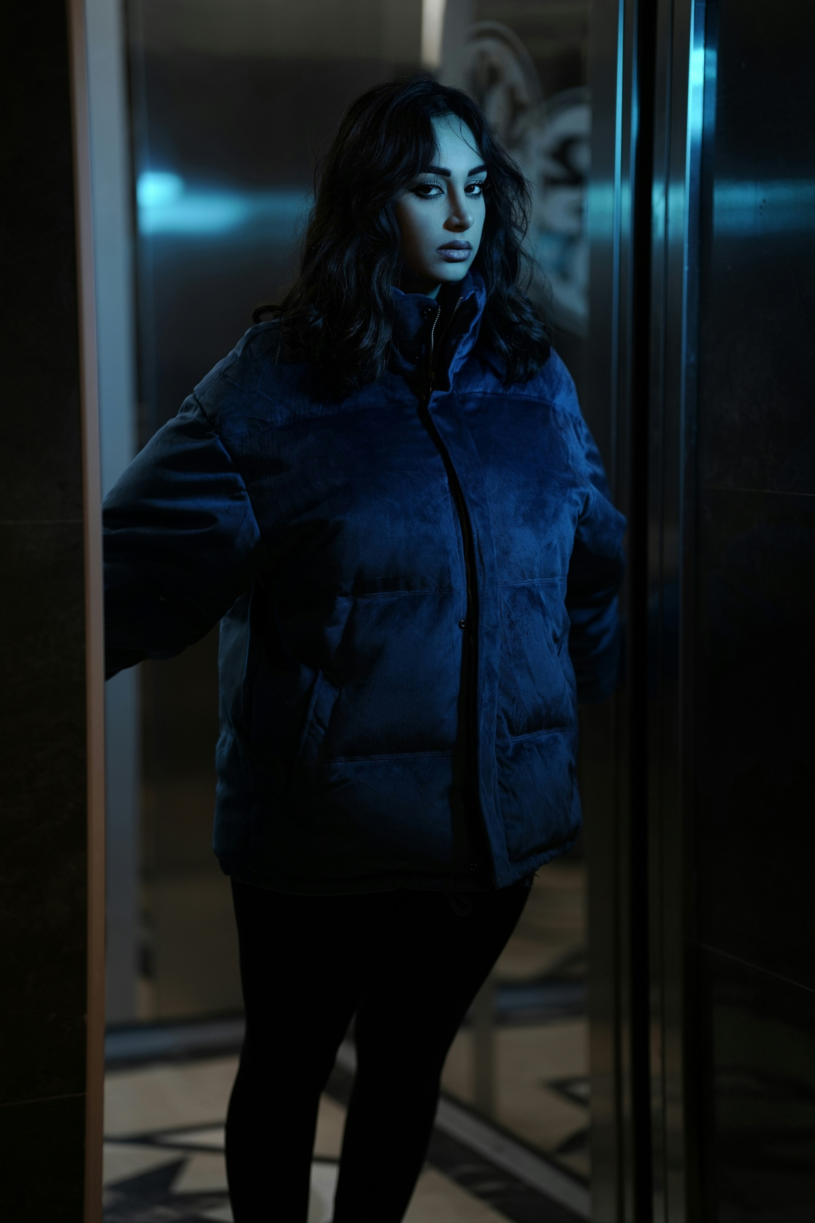 Woman in a blue puffer jacket inside an elevator.