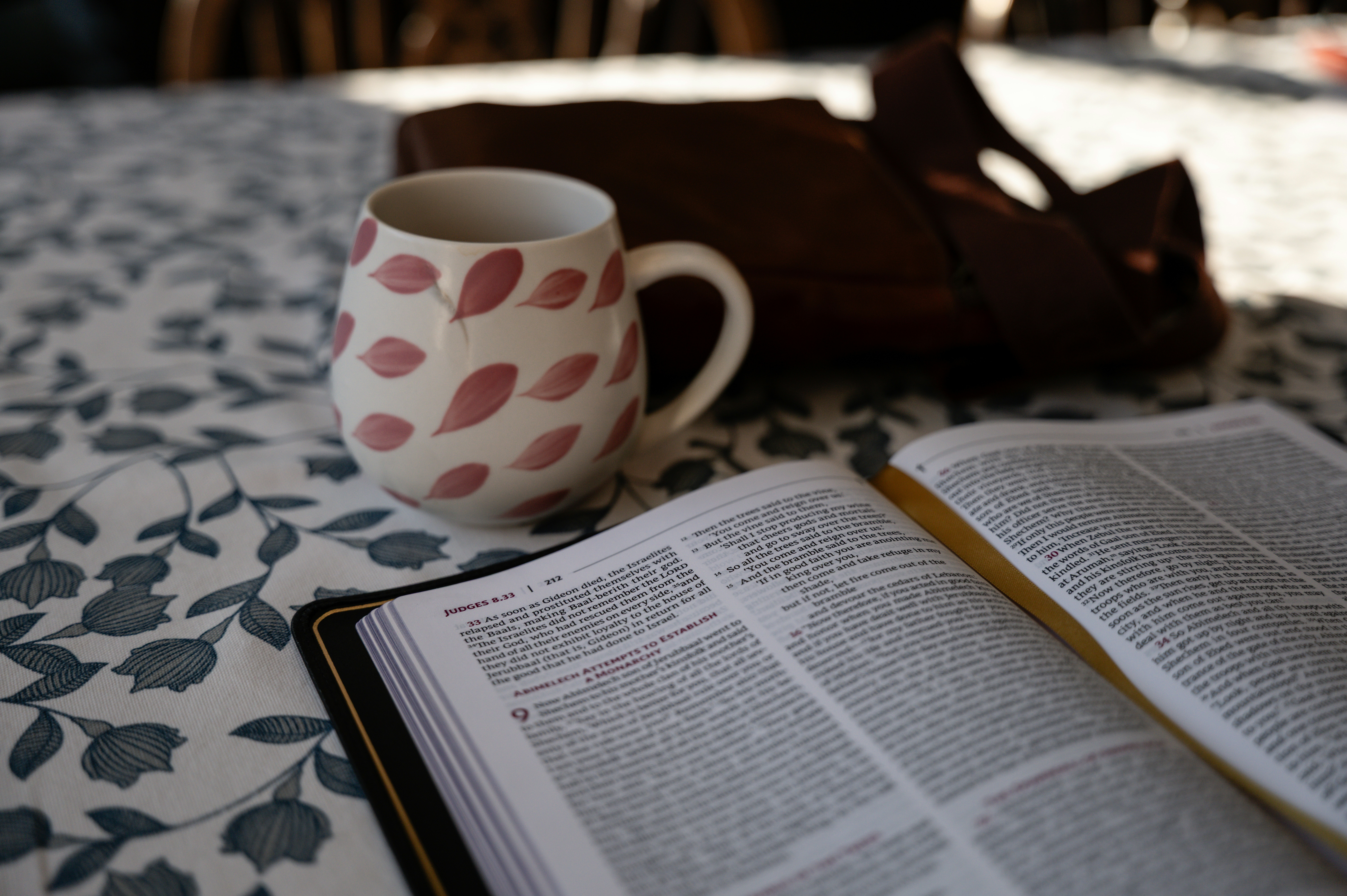 A mug and open book on a patterned tablecloth.