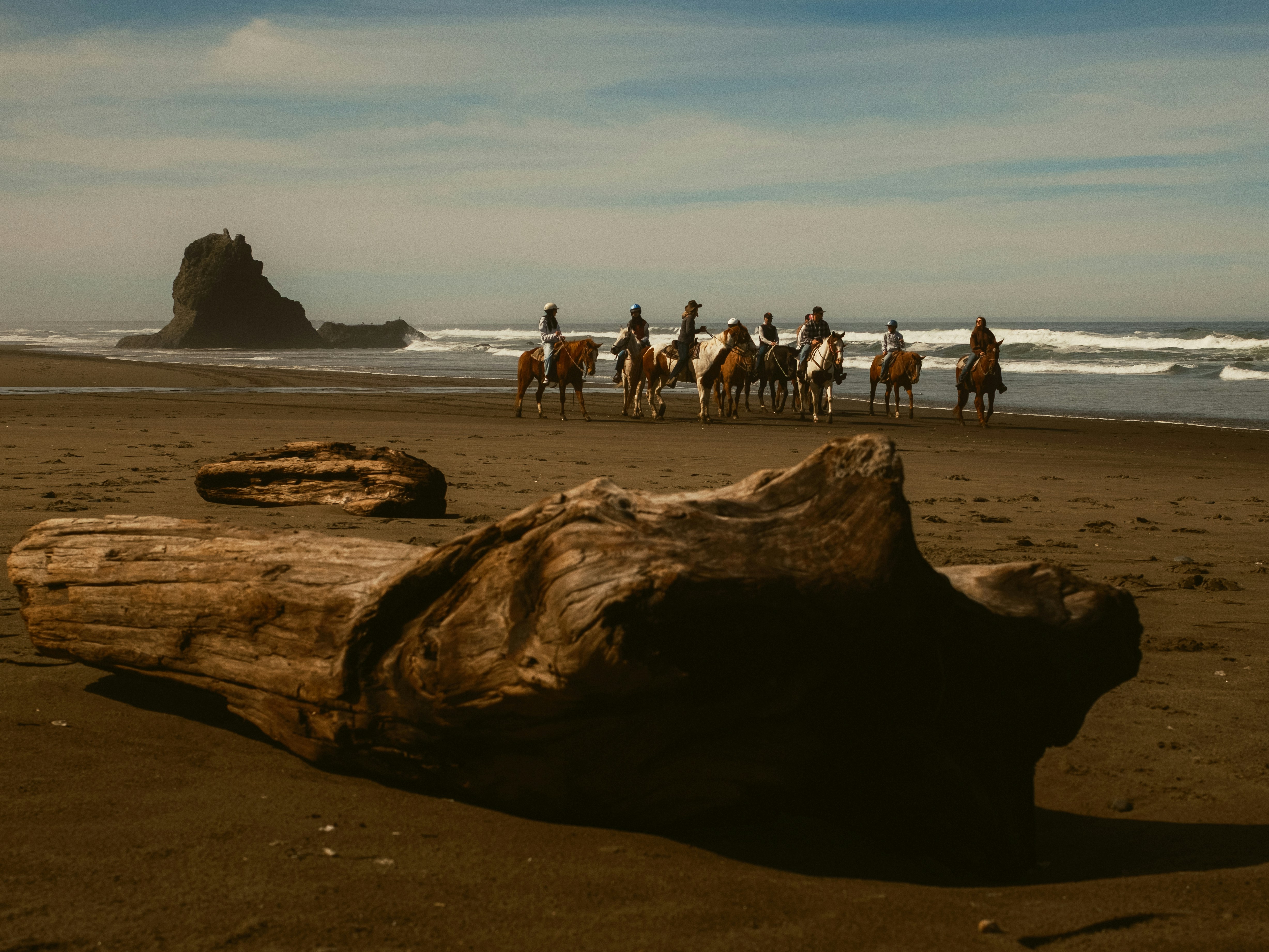 A group of people ride horses along a sandy beach.