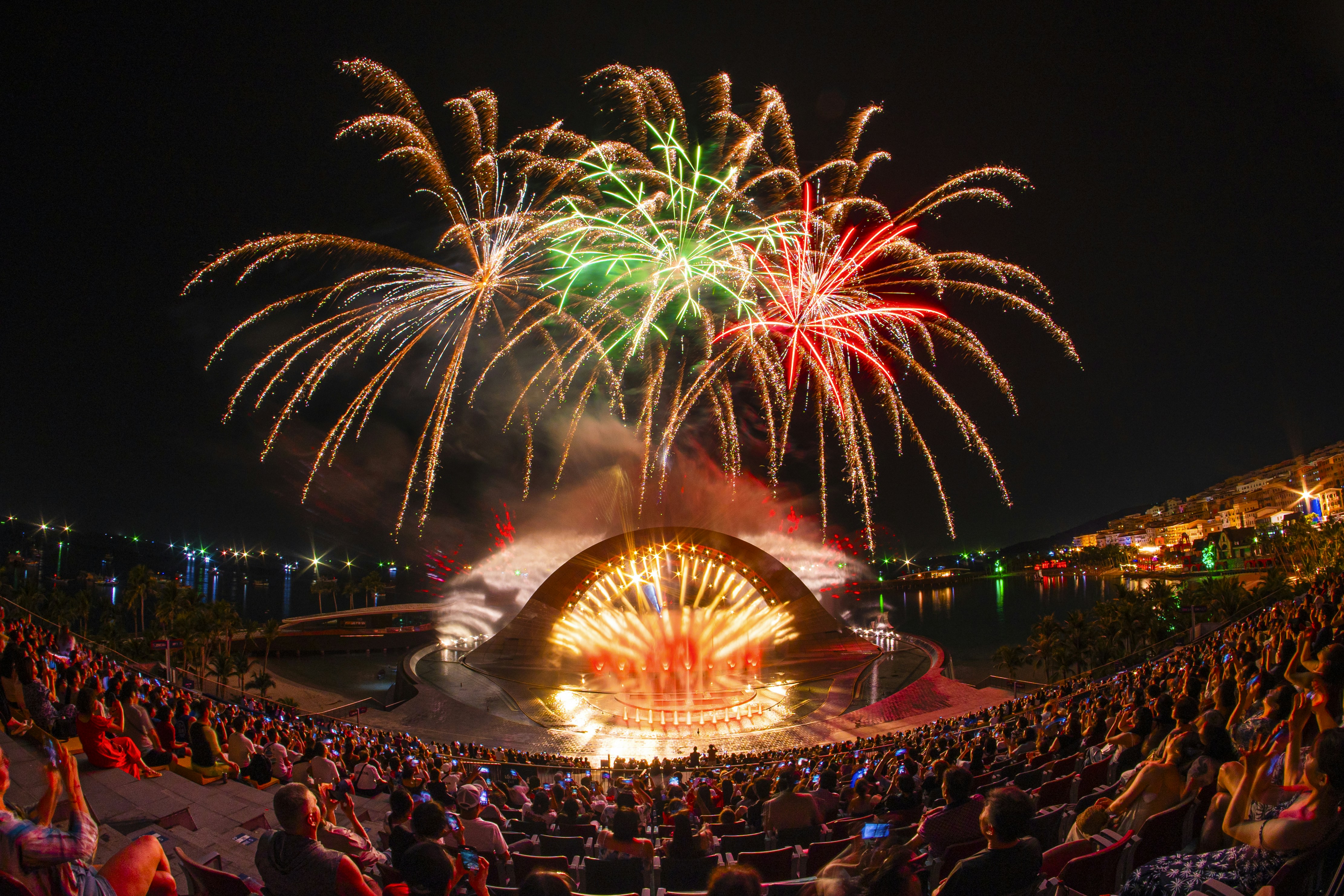 Fogos de artifício iluminam o céu noturno sobre uma multidão aplaudindo.