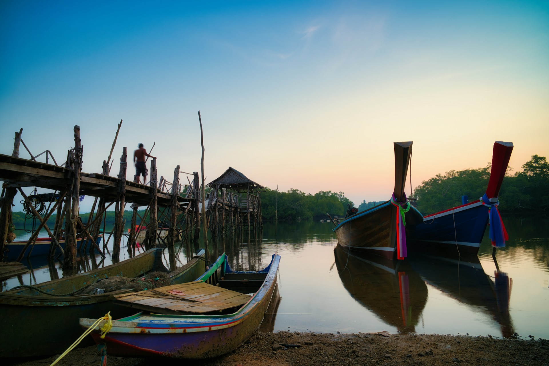 Longtail boats moored at wooden pier at sunset