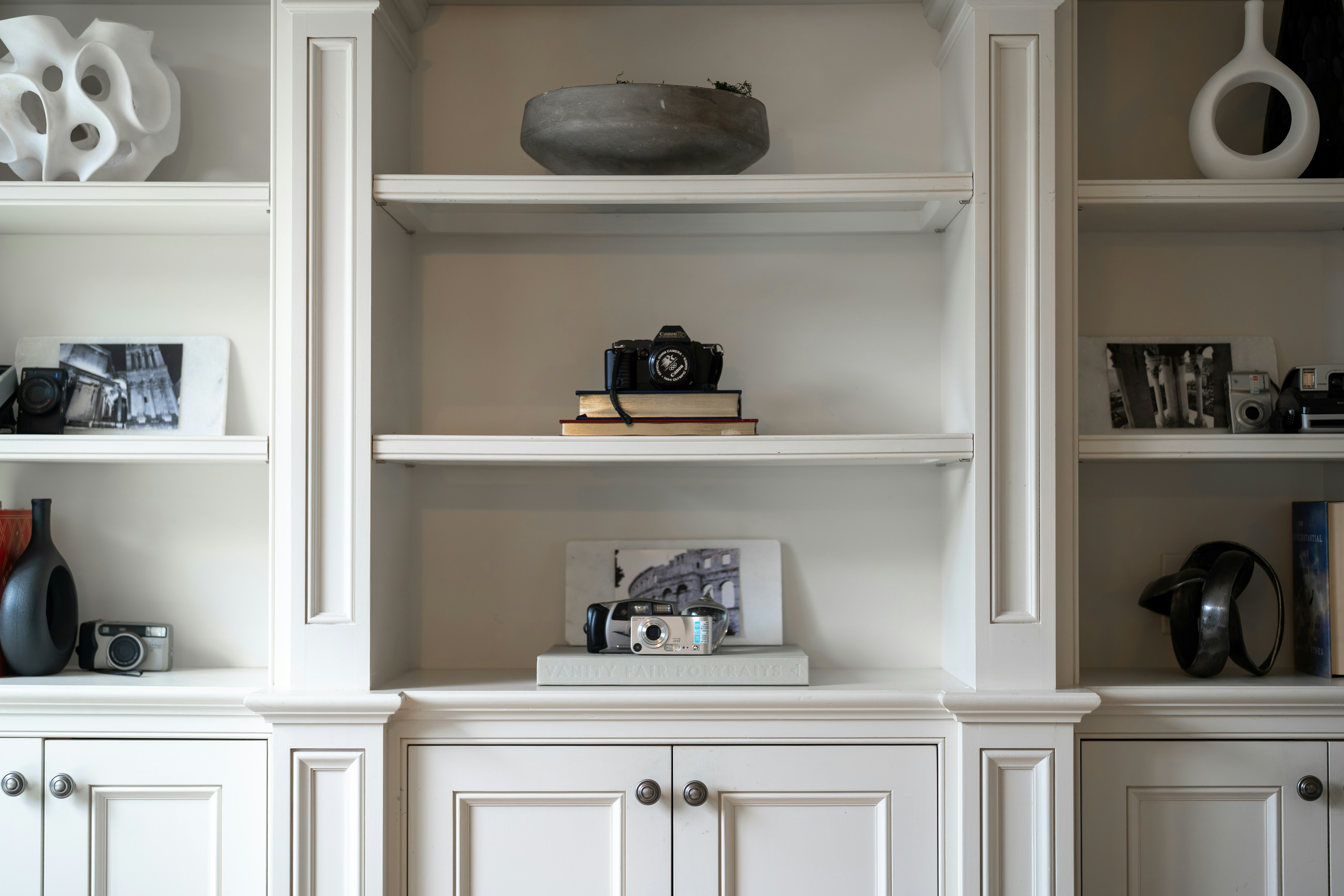 Des étagères blanches intégrées exposent des objets décoratifs et des appareils photo.