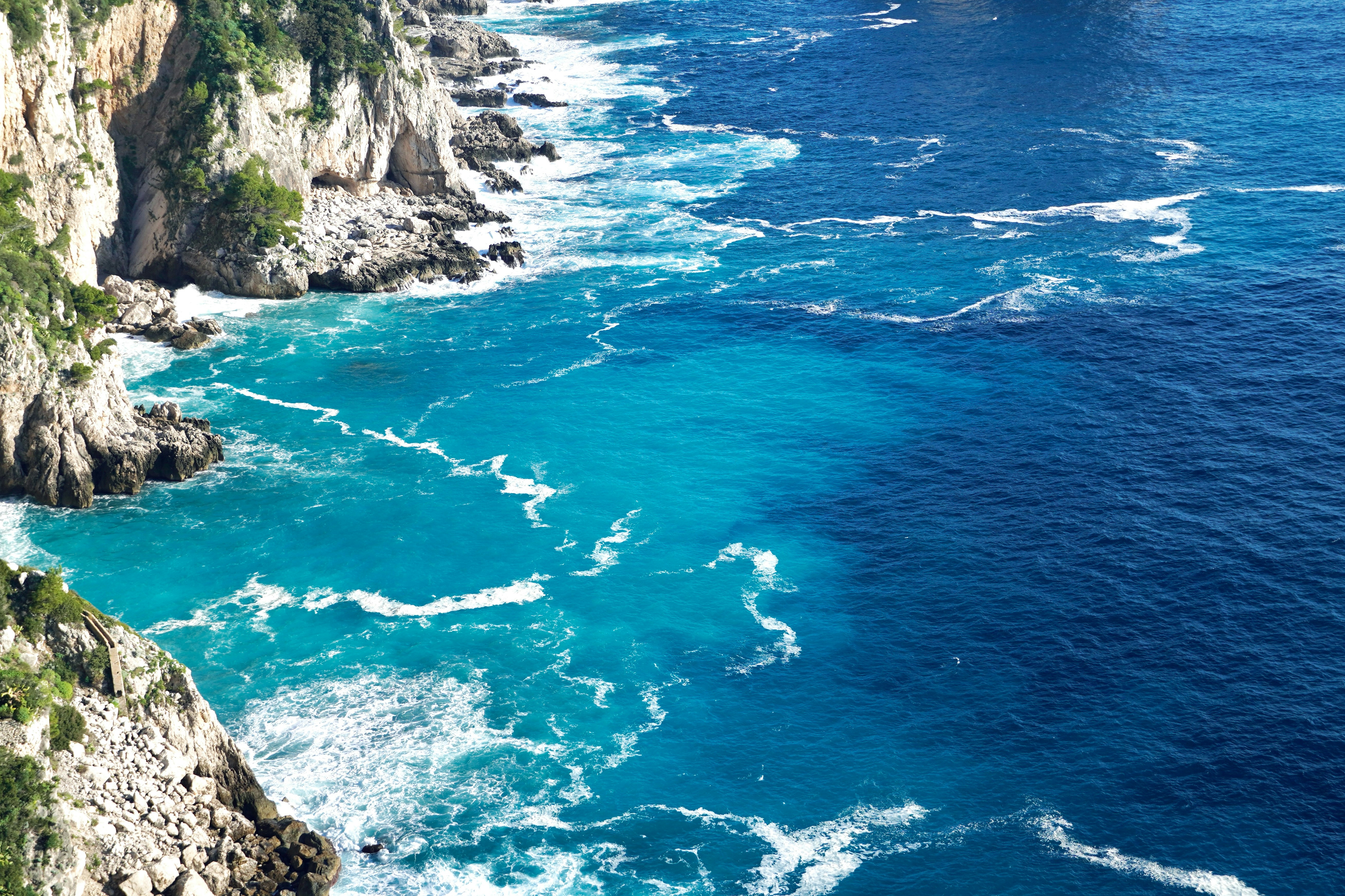 Las olas turquesas del océano rompen contra acantilados rocosos.