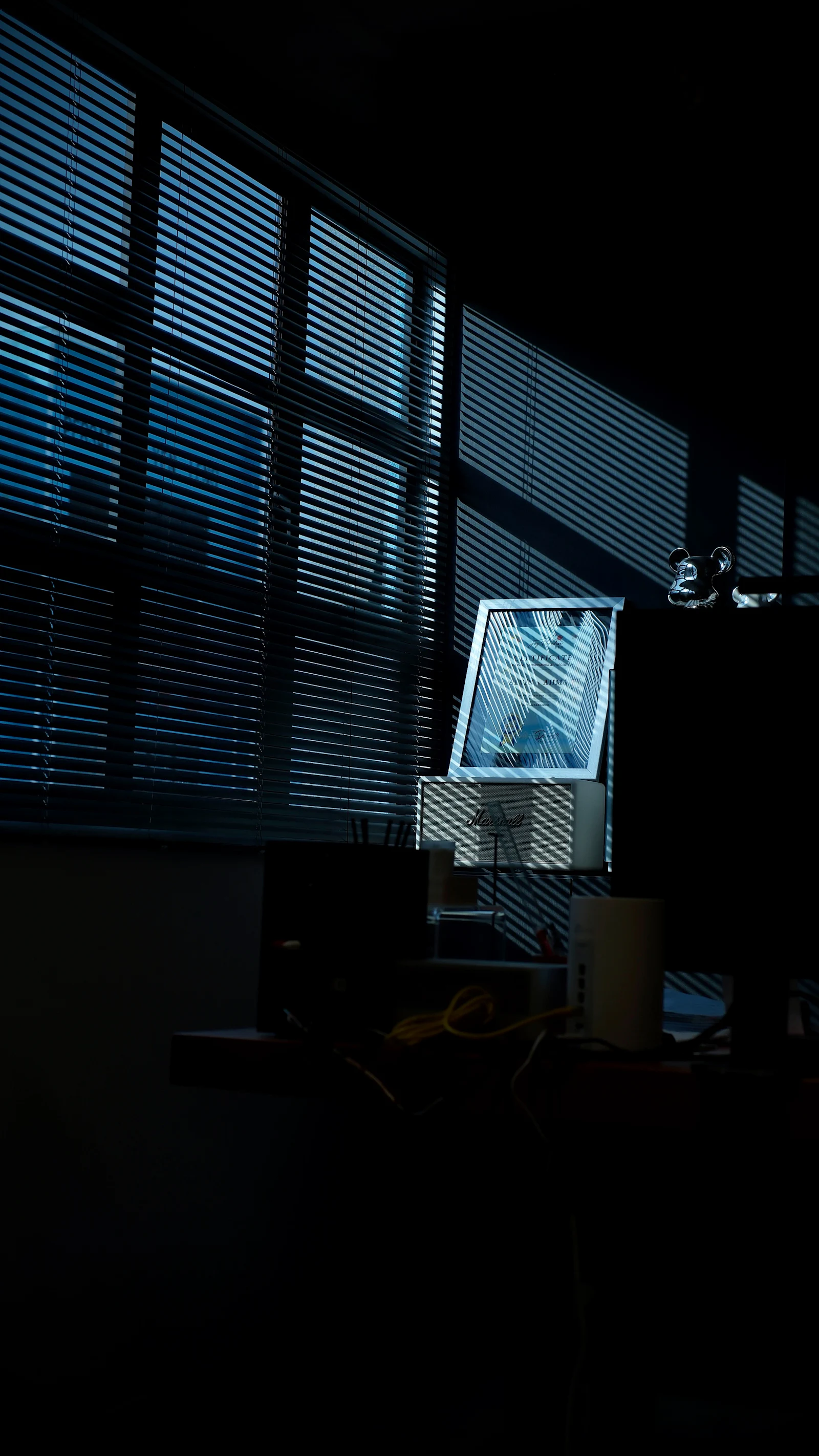 Light through half closed blinds falling in stripes across a desk.