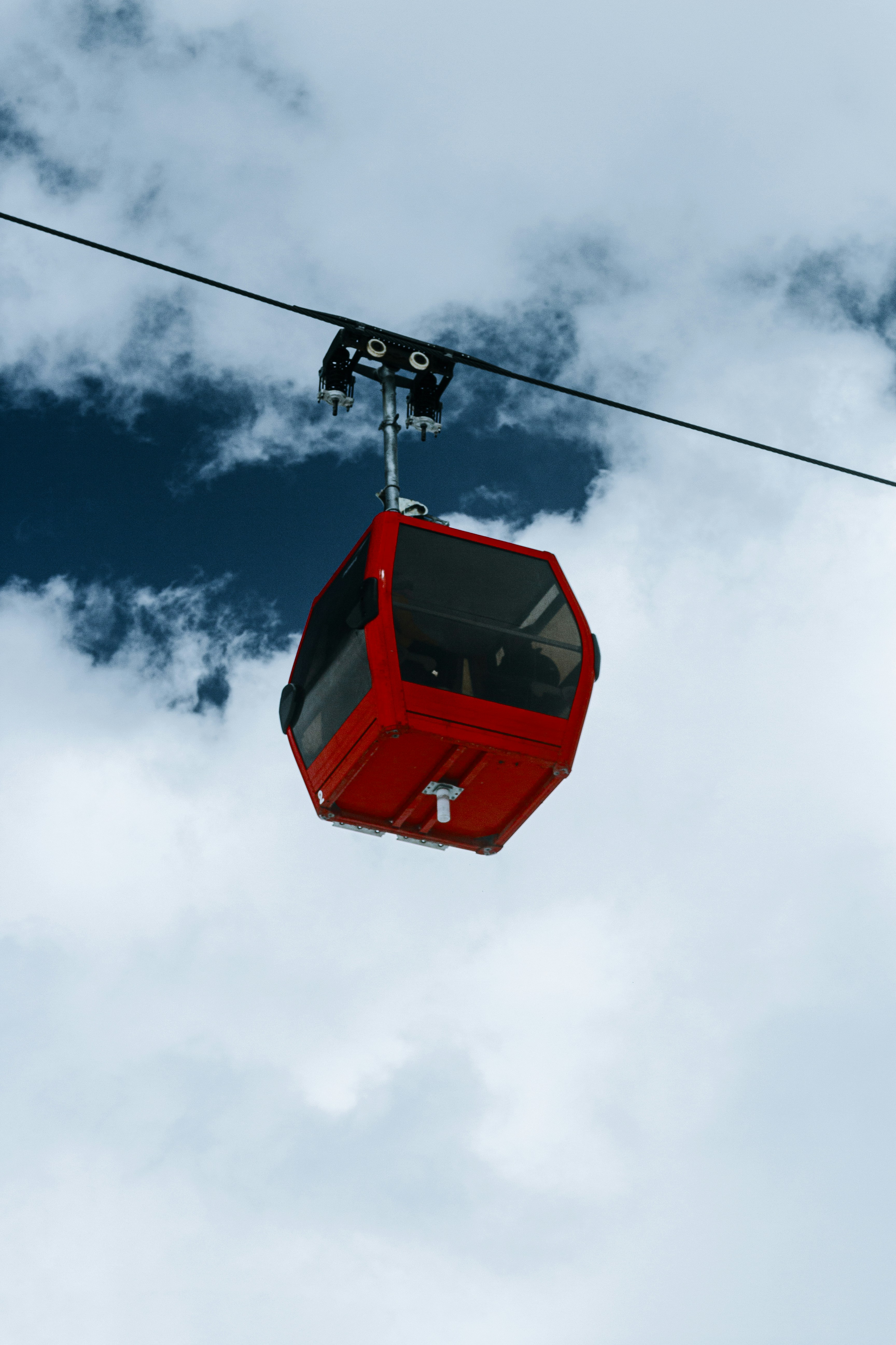 A red cable car ascends a cloudy sky.