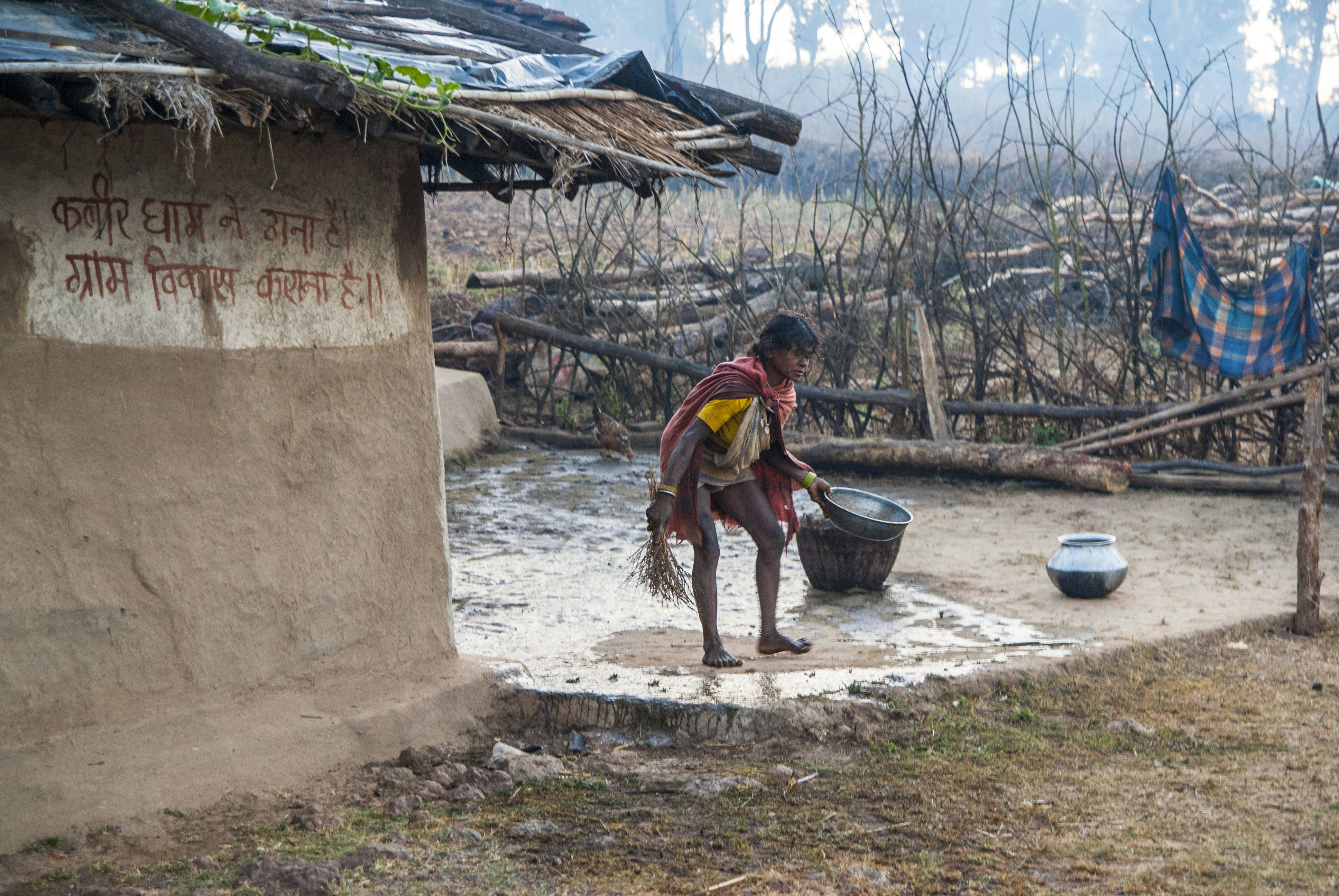 A person collecting water from a well near a hut.