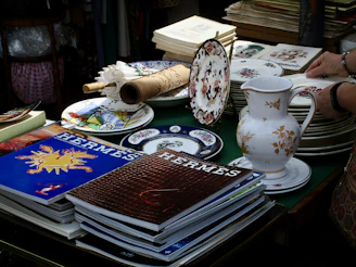 Stacks of hermes magazines and decorative plates on table.