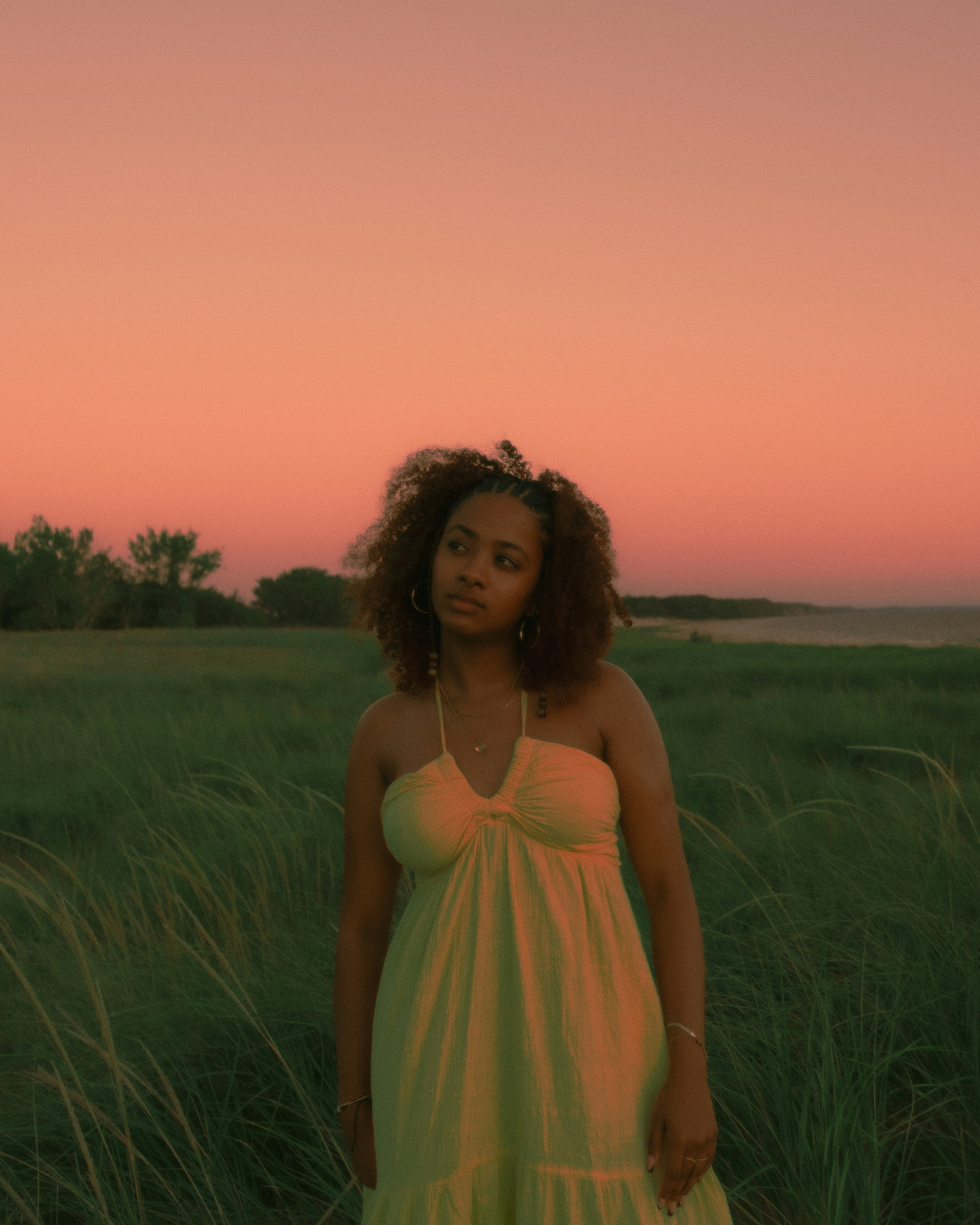 Woman in yellow dress stands in grassy field at sunset