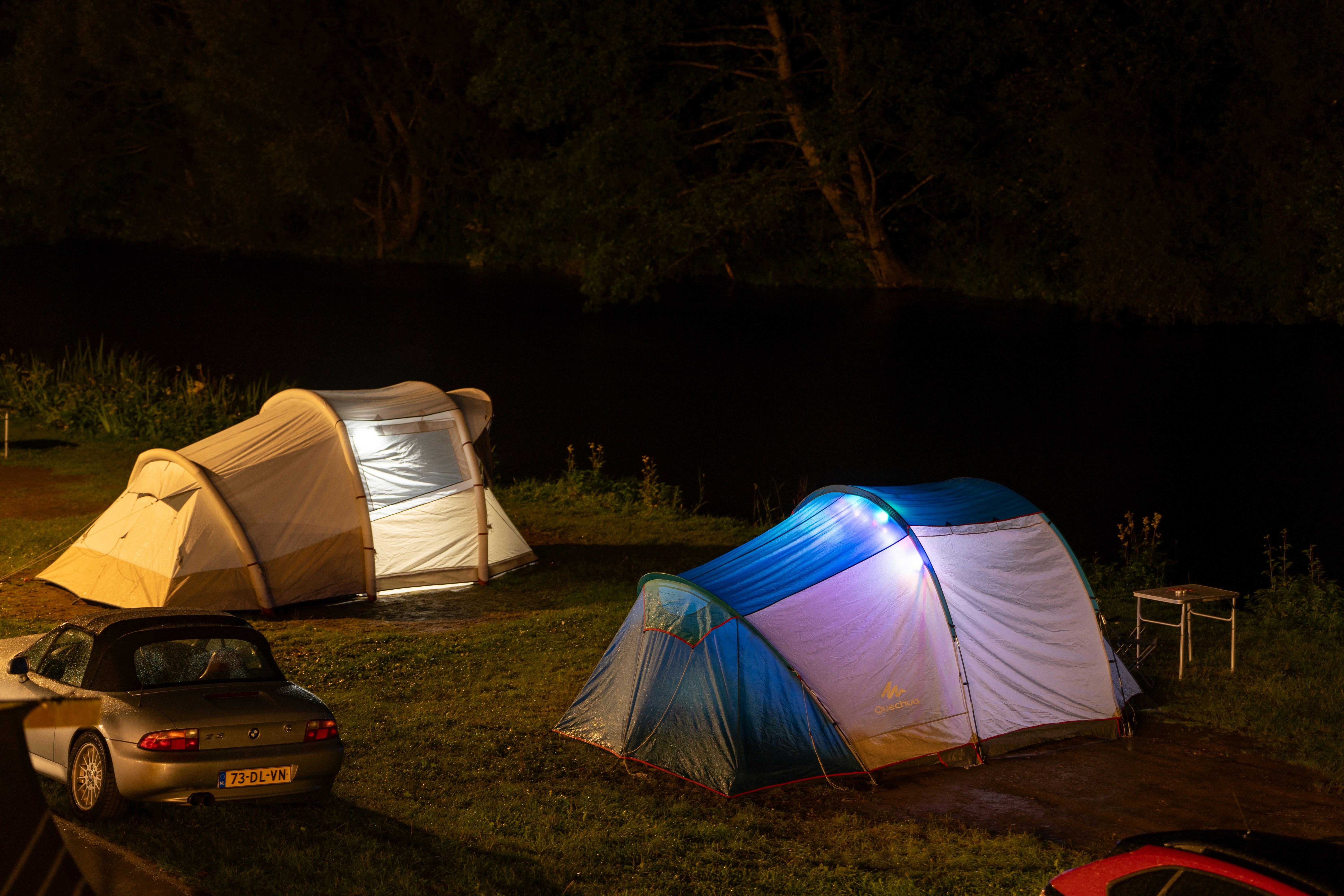 Tents illuminated at night with a car nearby