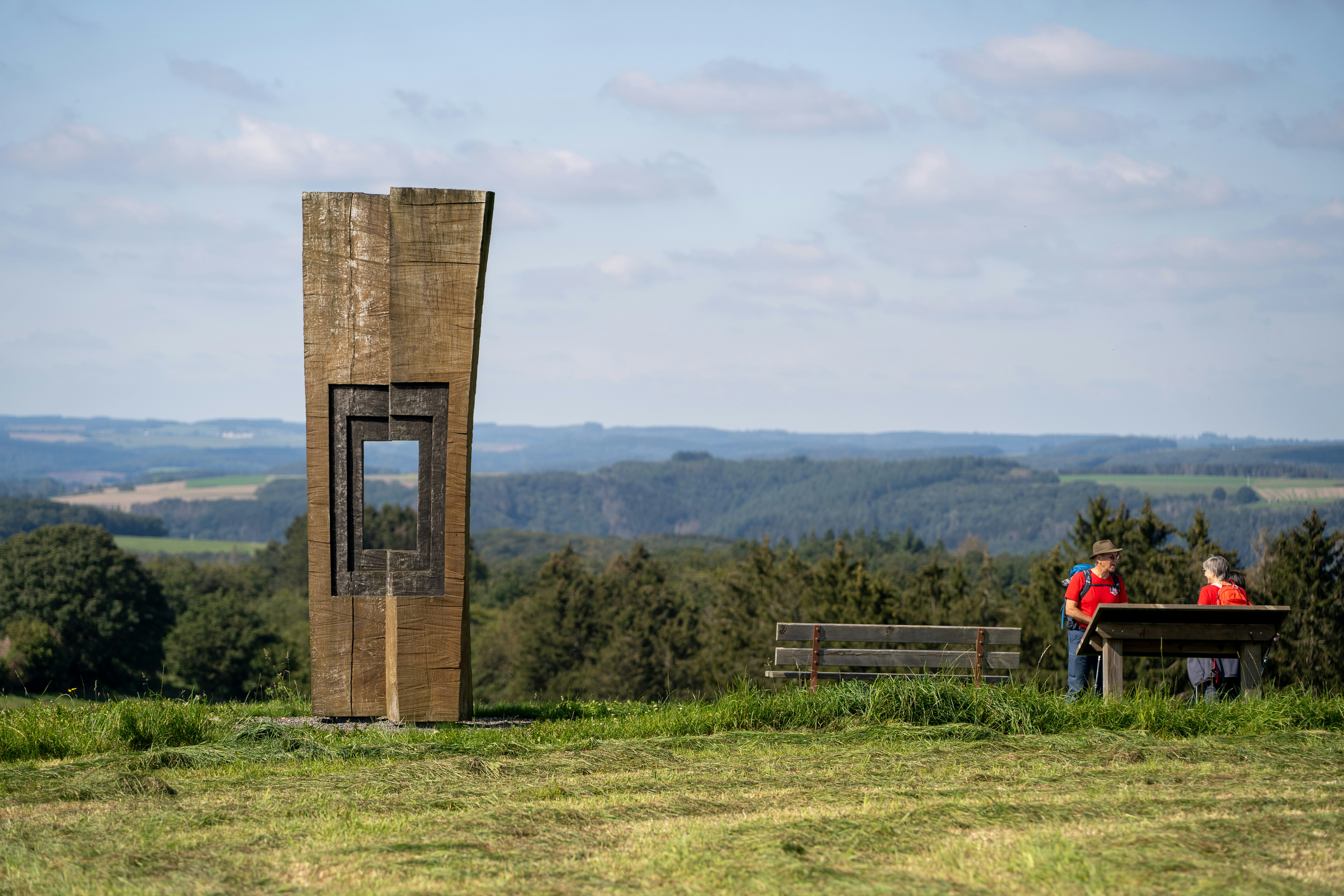 Zwei Personen bewundern eine moderne Skulptur mit Blick auf sanfte Hügel.