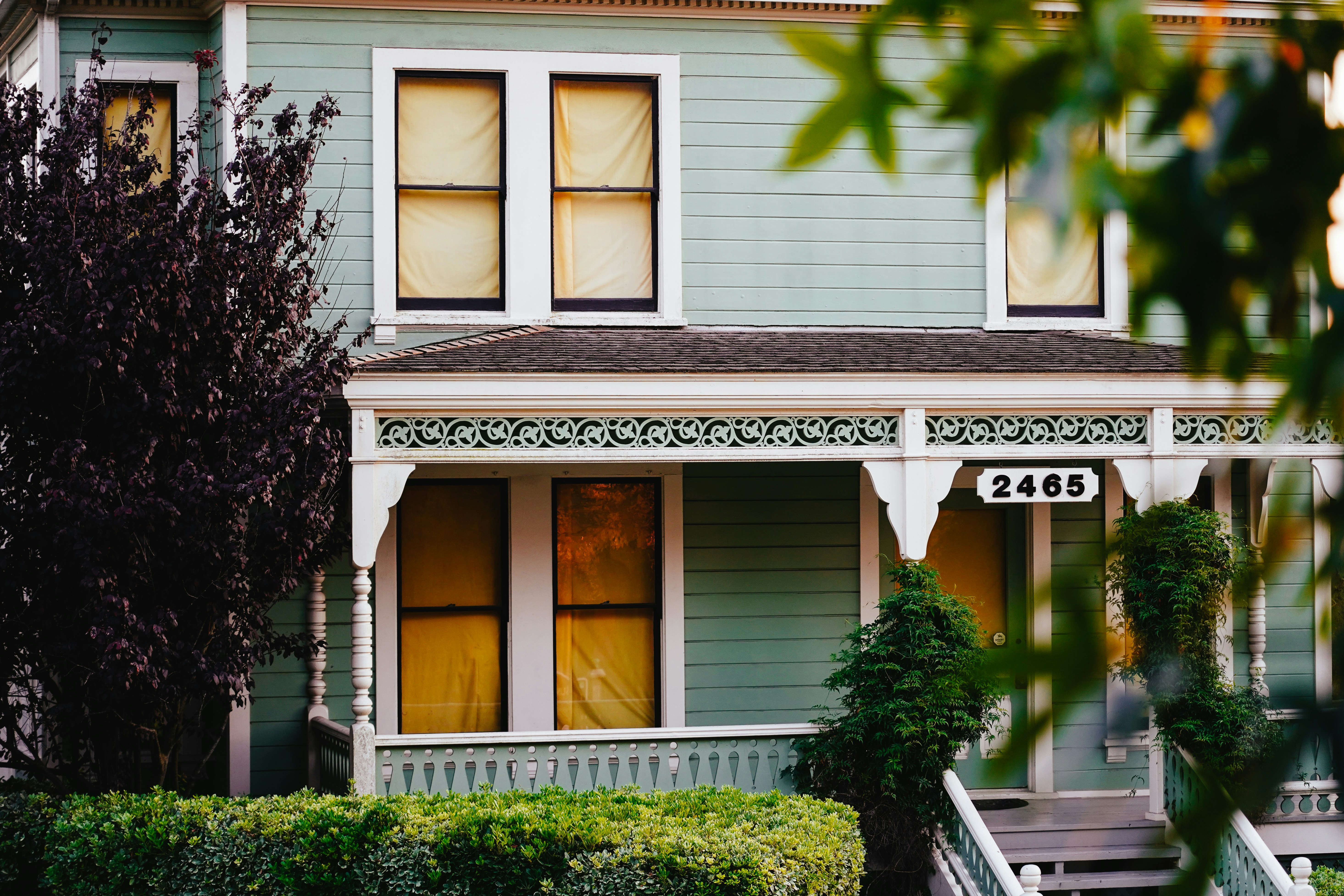 A light blue house with a porch and green bushes.