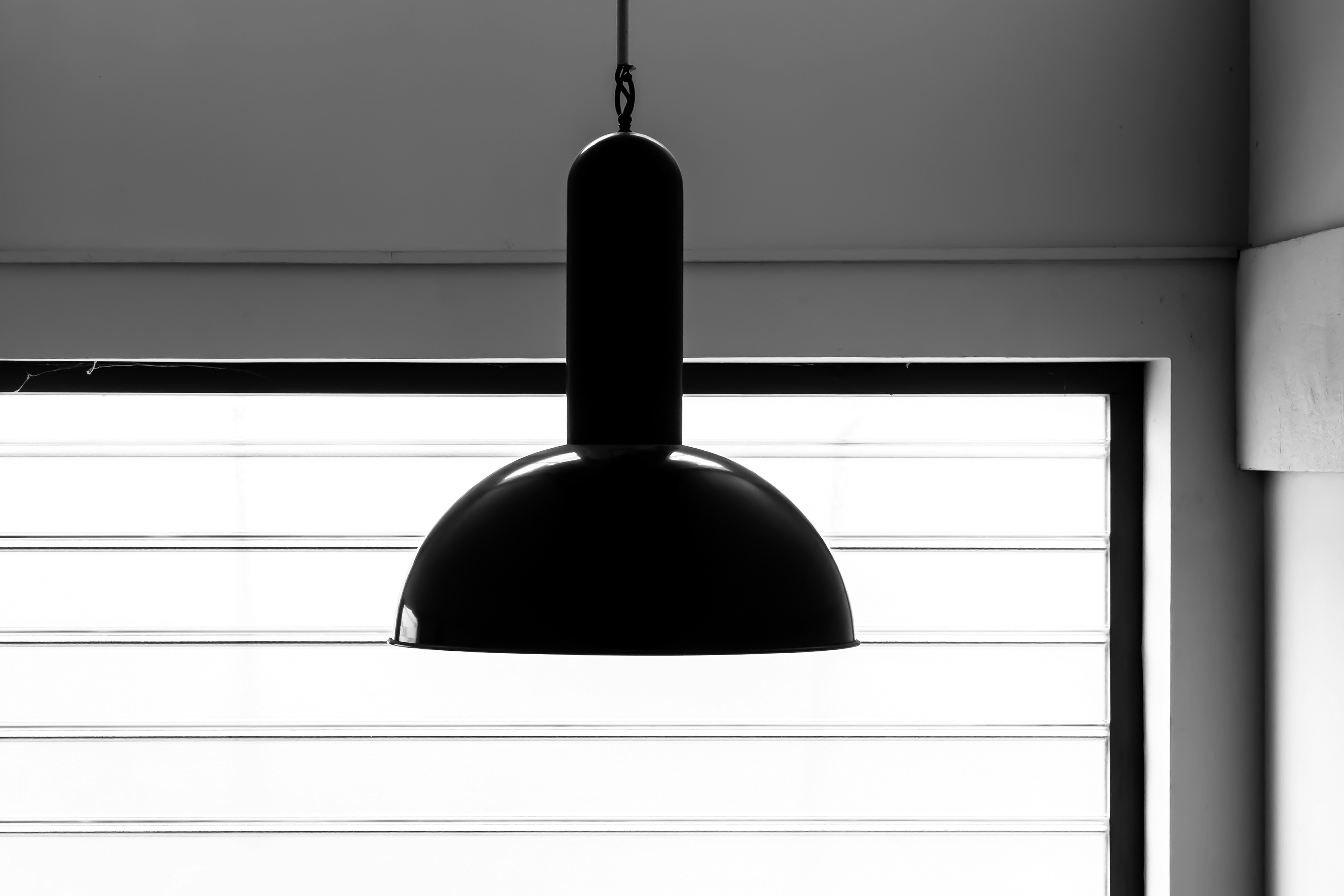 Black pendant lamp hanging in front of blinds.