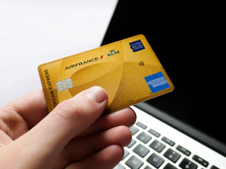 Hand holding a gold american express card near laptop