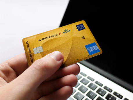 Hand holding a gold american express card near laptop