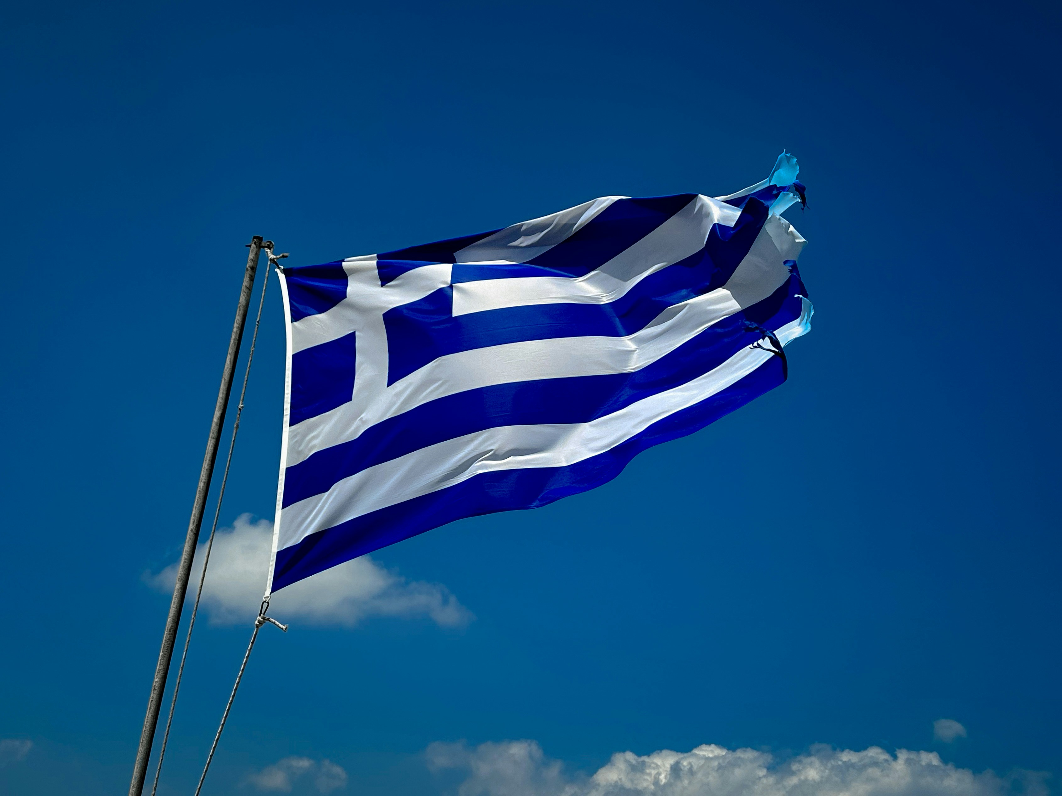 A bandeira grega tremula contra um céu azul.