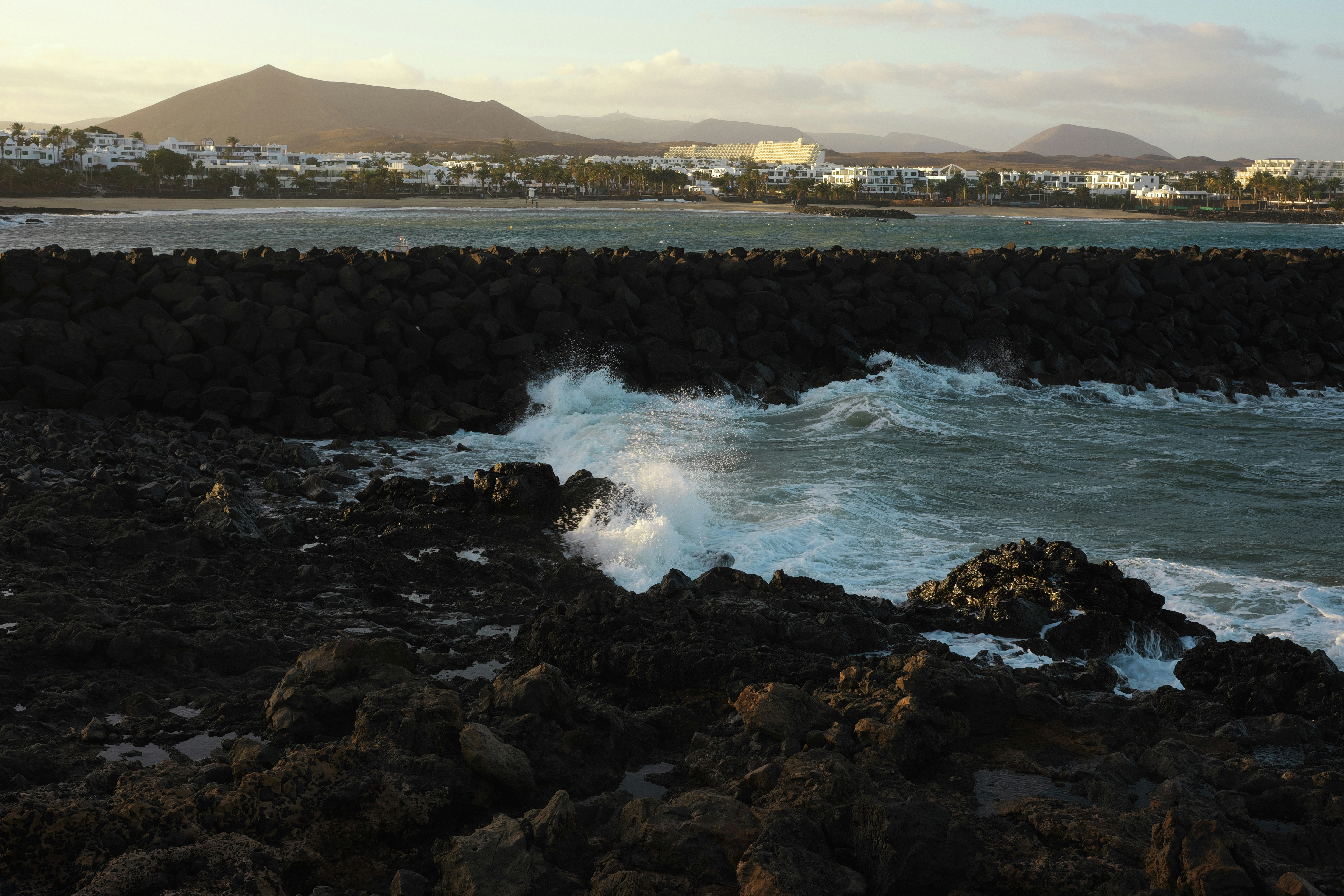 Fotomural Waves crashing against rocks with a town in background