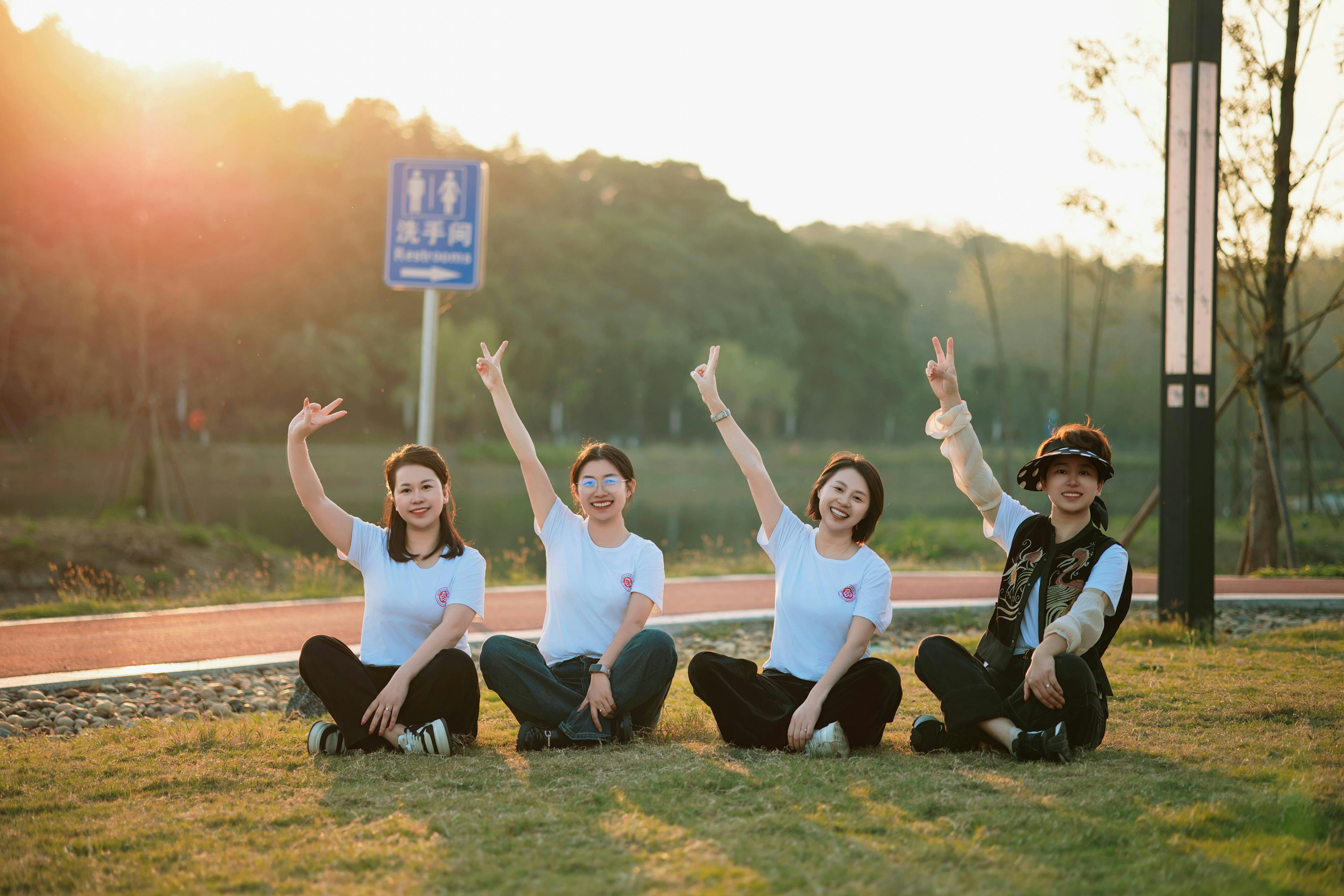 Four women sitting on grass with arms raised