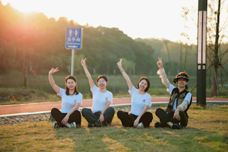 Four women sitting on grass with arms raised