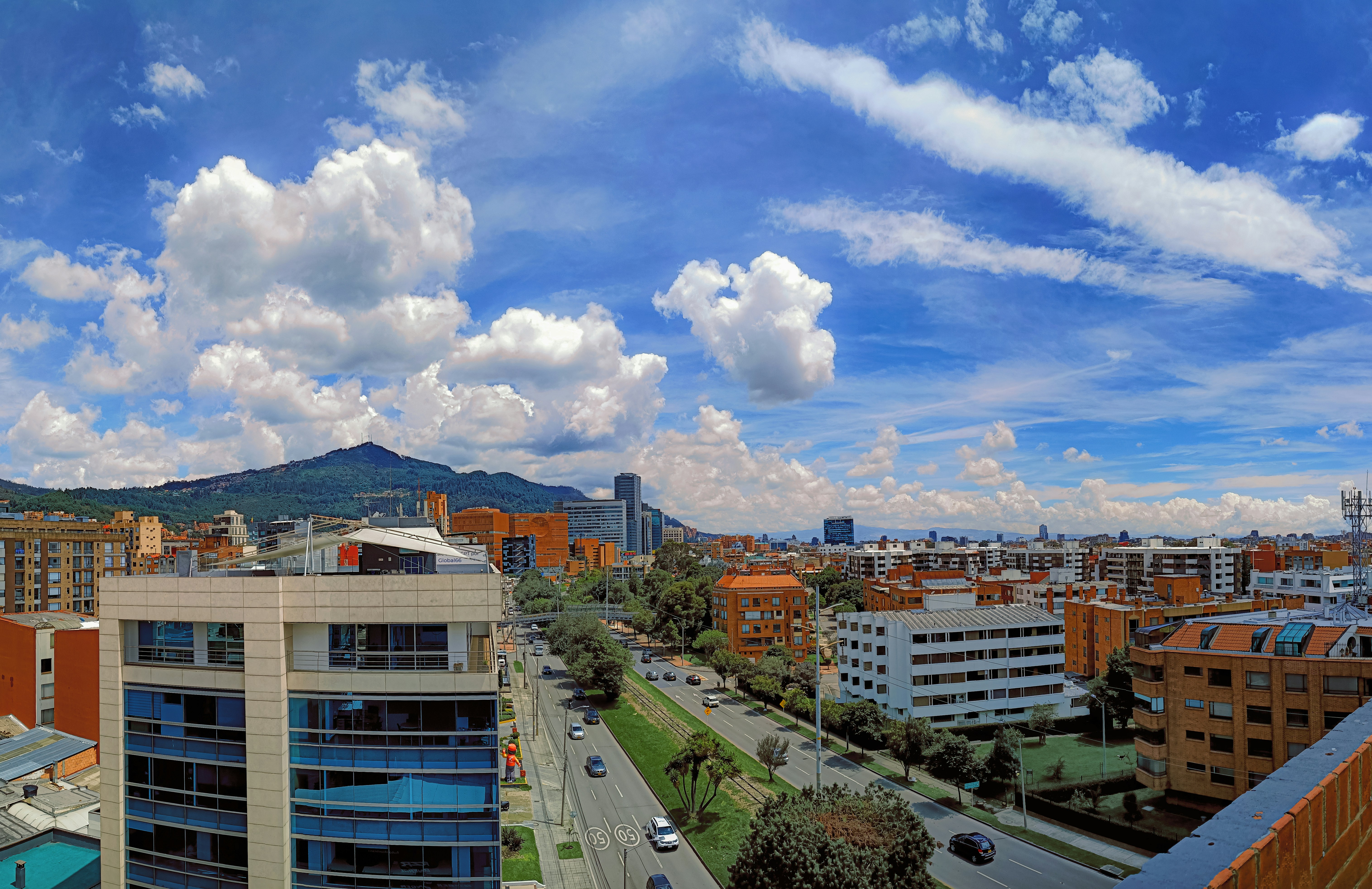 Paisaje urbano con edificios, carreteras y montañas lejanas bajo las nubes.