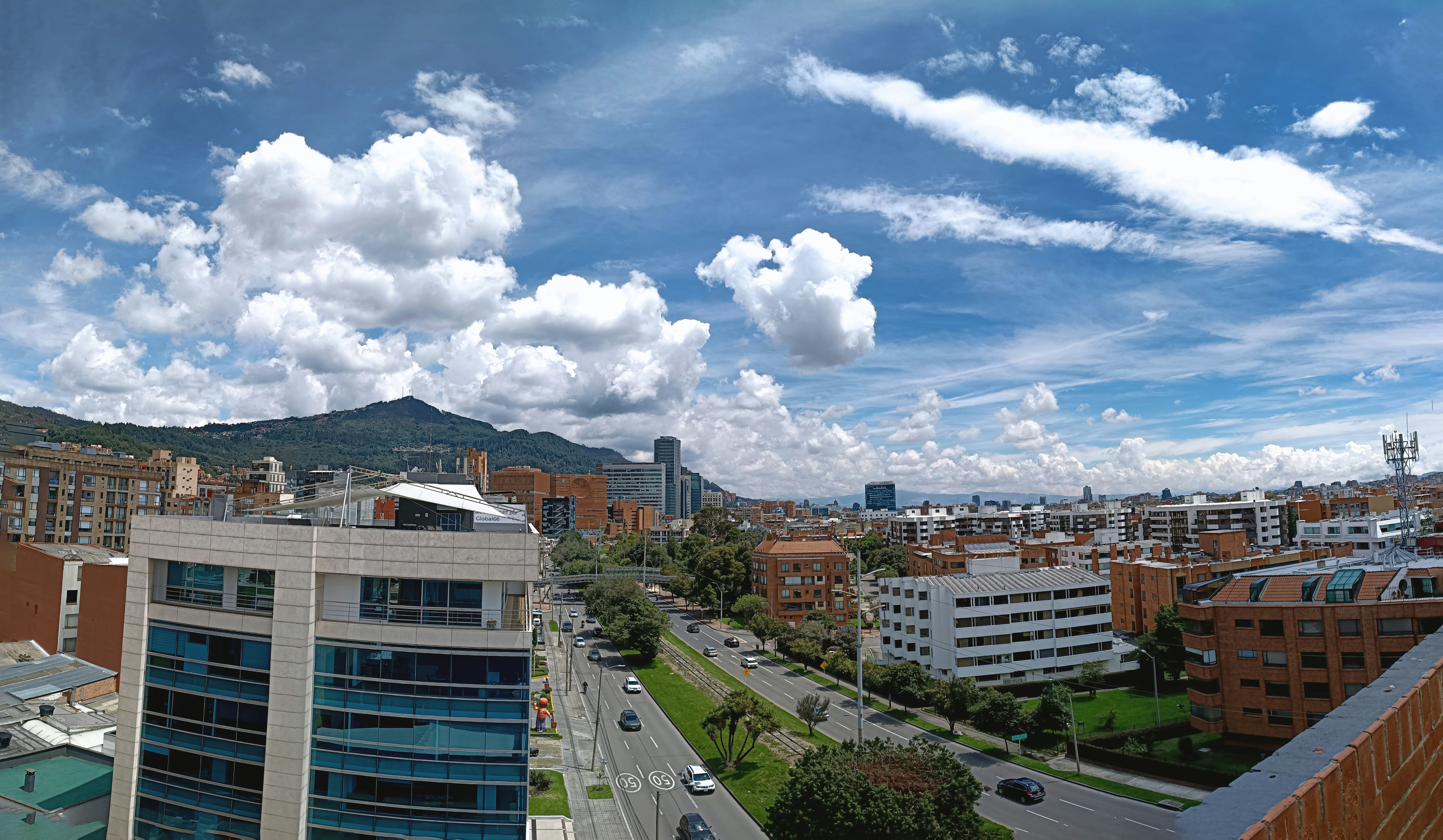Paisaje urbano con edificios, carreteras y montañas bajo un cielo azul.