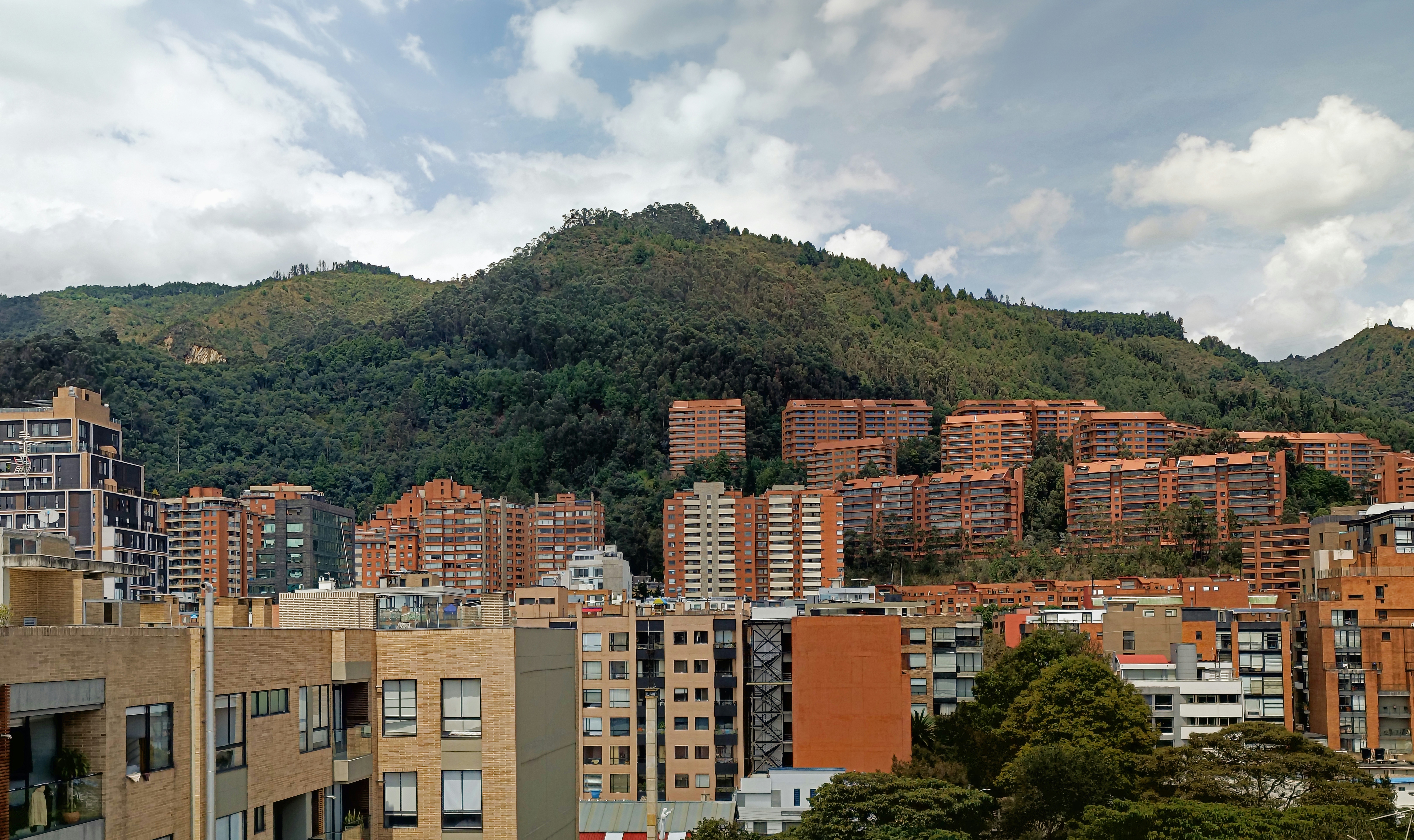 Edificios de apartamentos enclavados contra una montaña verde cubierta de árboles.