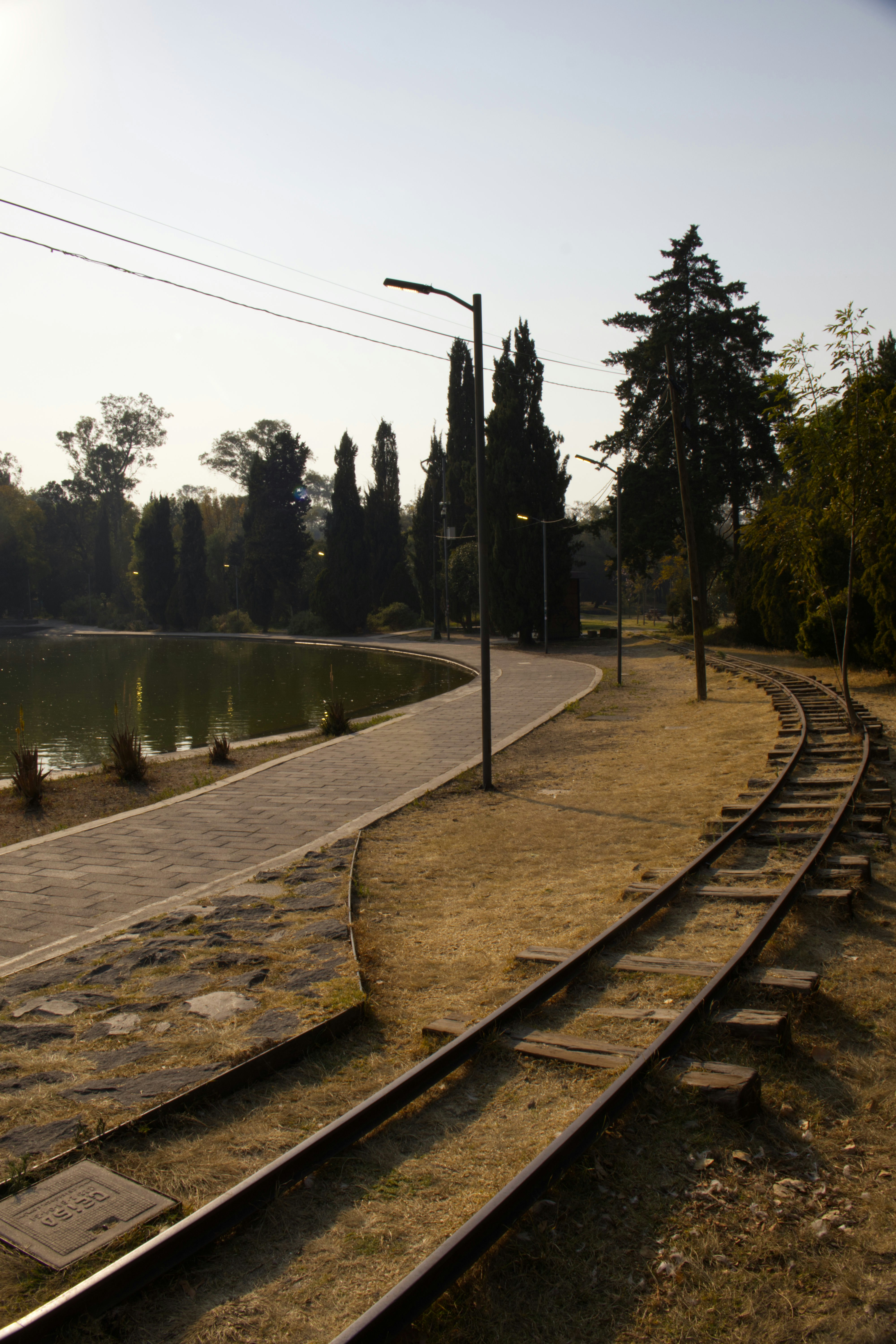 Train tracks curve beside a park lake and pathway.