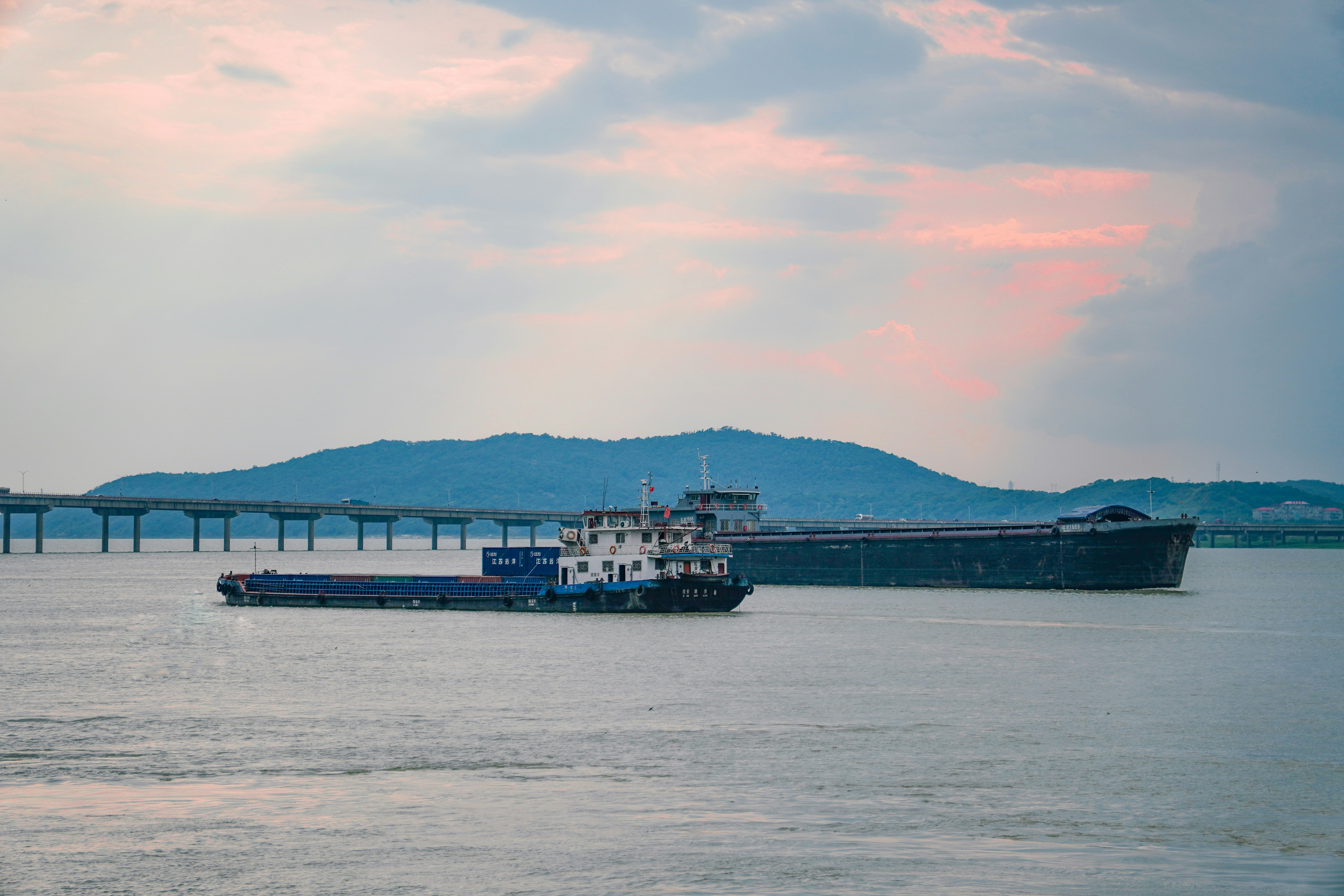 Two cargo ships sail on the water near a bridge.