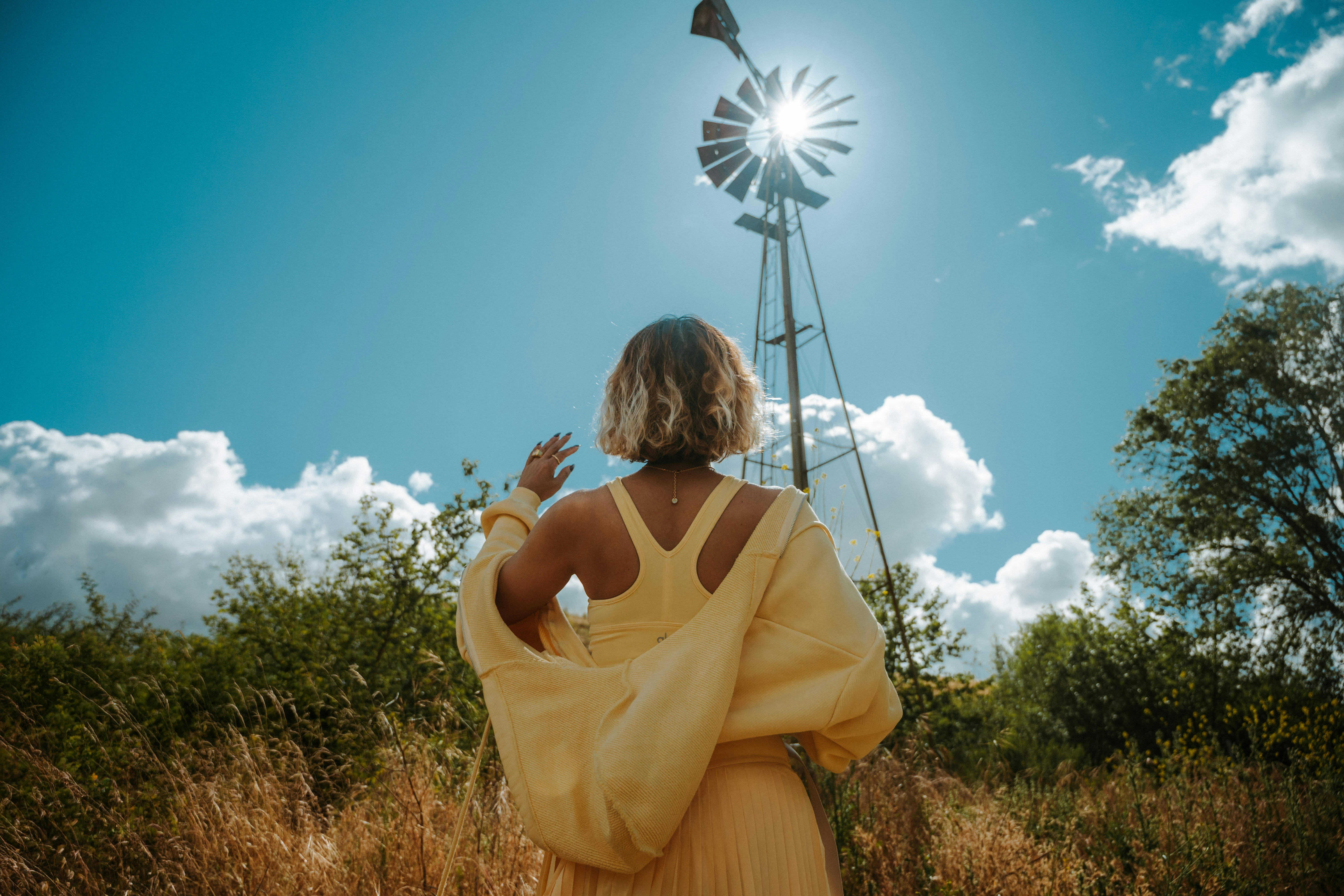 Frau im gelben Kleid nahe der alten Windmühle unter strahlender Sonne