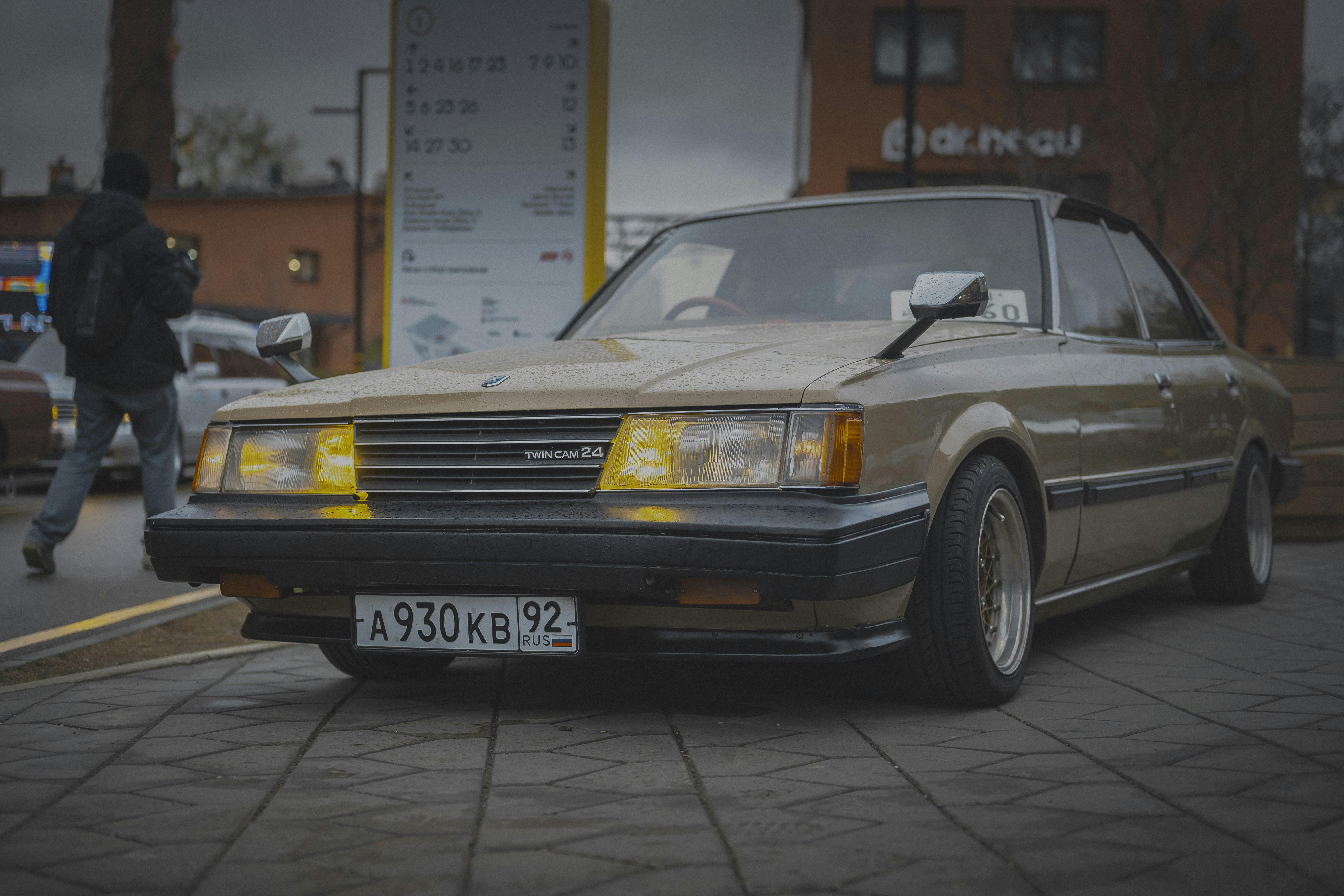 A classic gold sedan parked on a brick street.