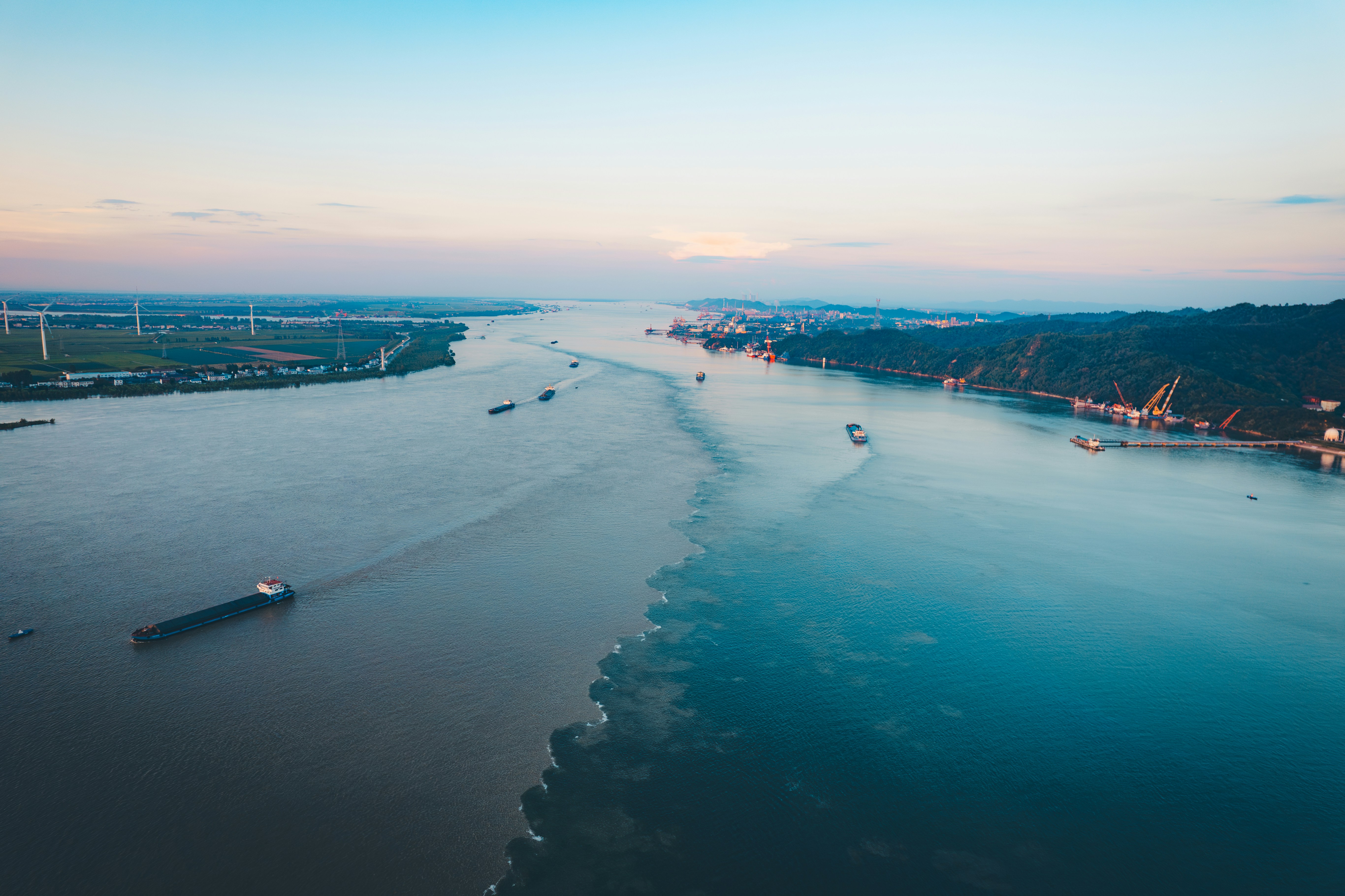 Cargo ships navigate a wide river at dusk.