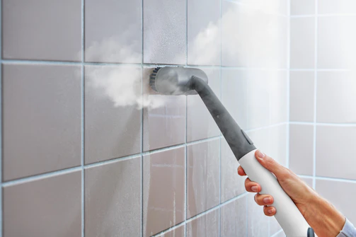 Steam cleaner sanitizing tiled wall in bathroom.