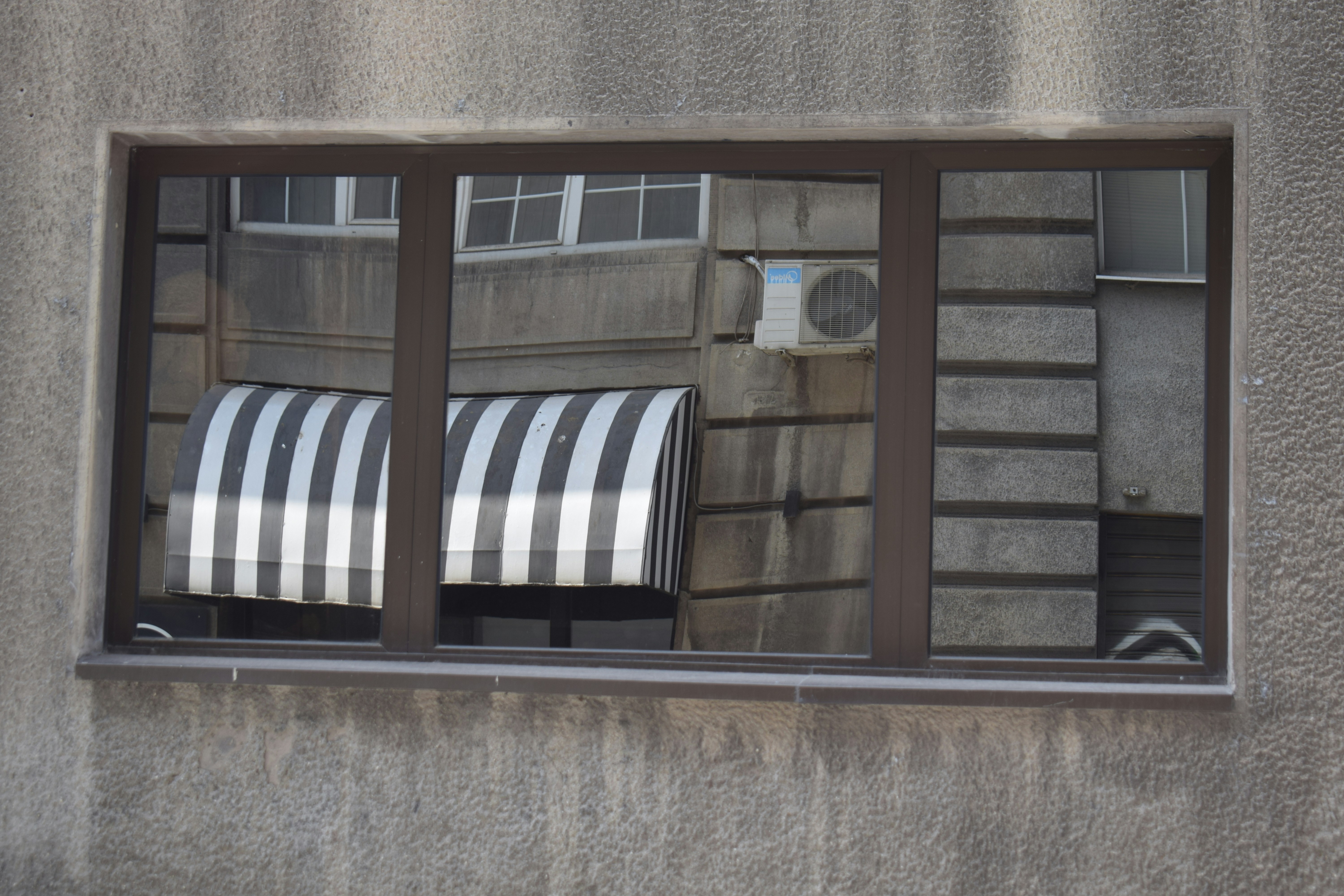 Reflection of striped awning and ac unit in window.