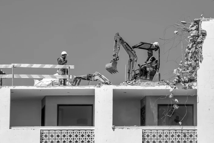 Workers demolishing a building with an excavator and hand tools