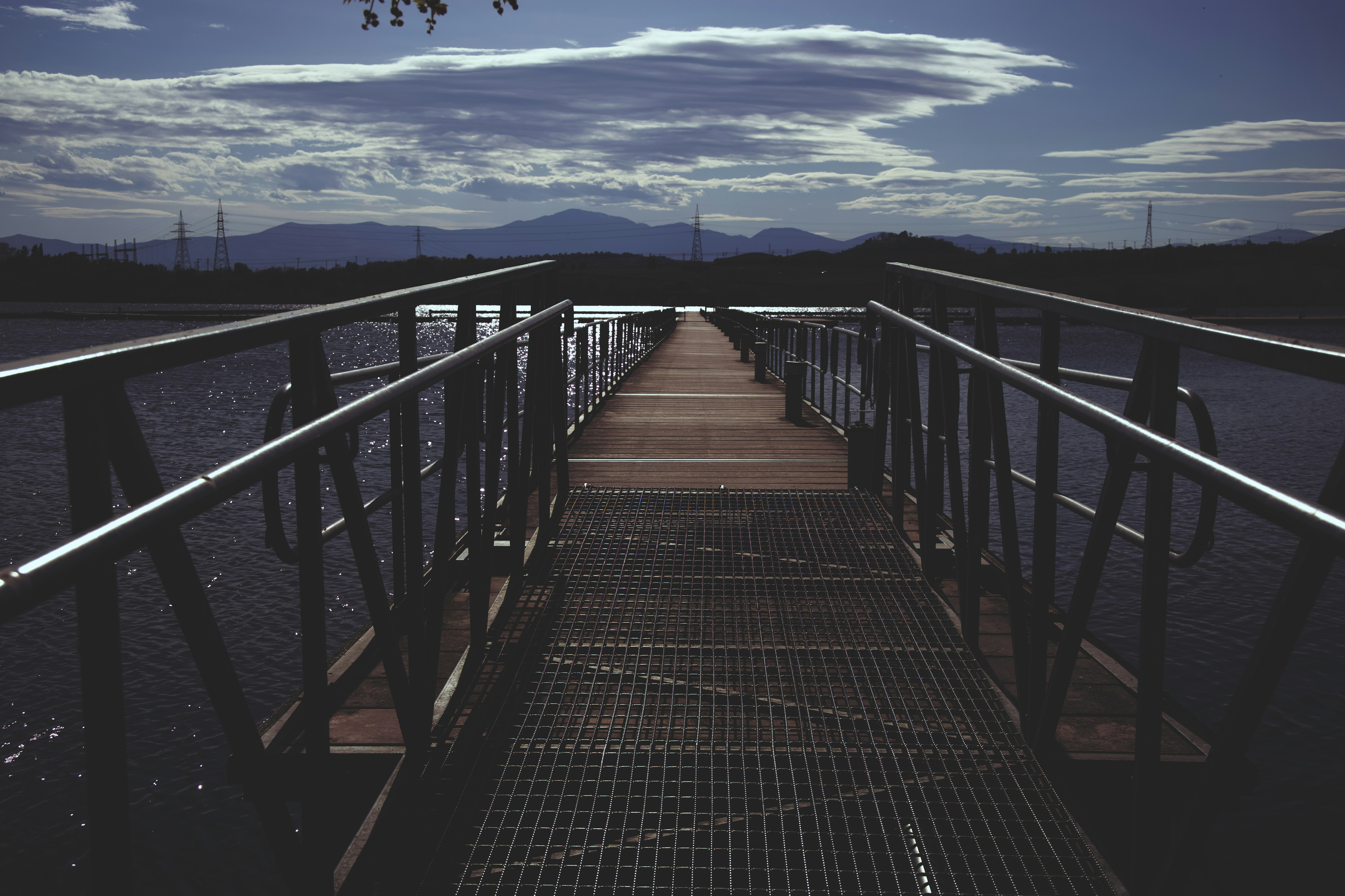 A long pier extends over the water towards mountains.