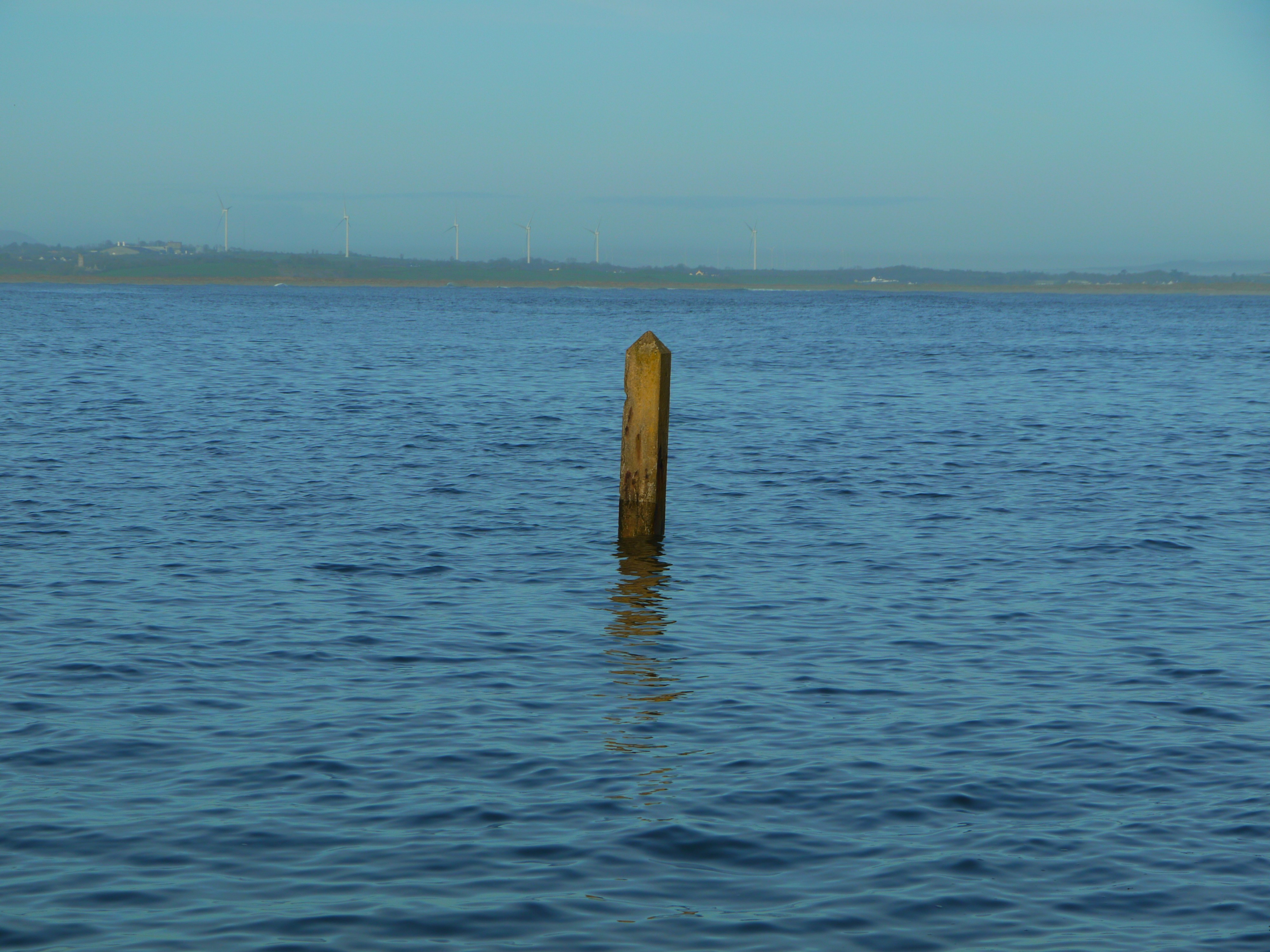 A single wooden post stands in the calm blue water.