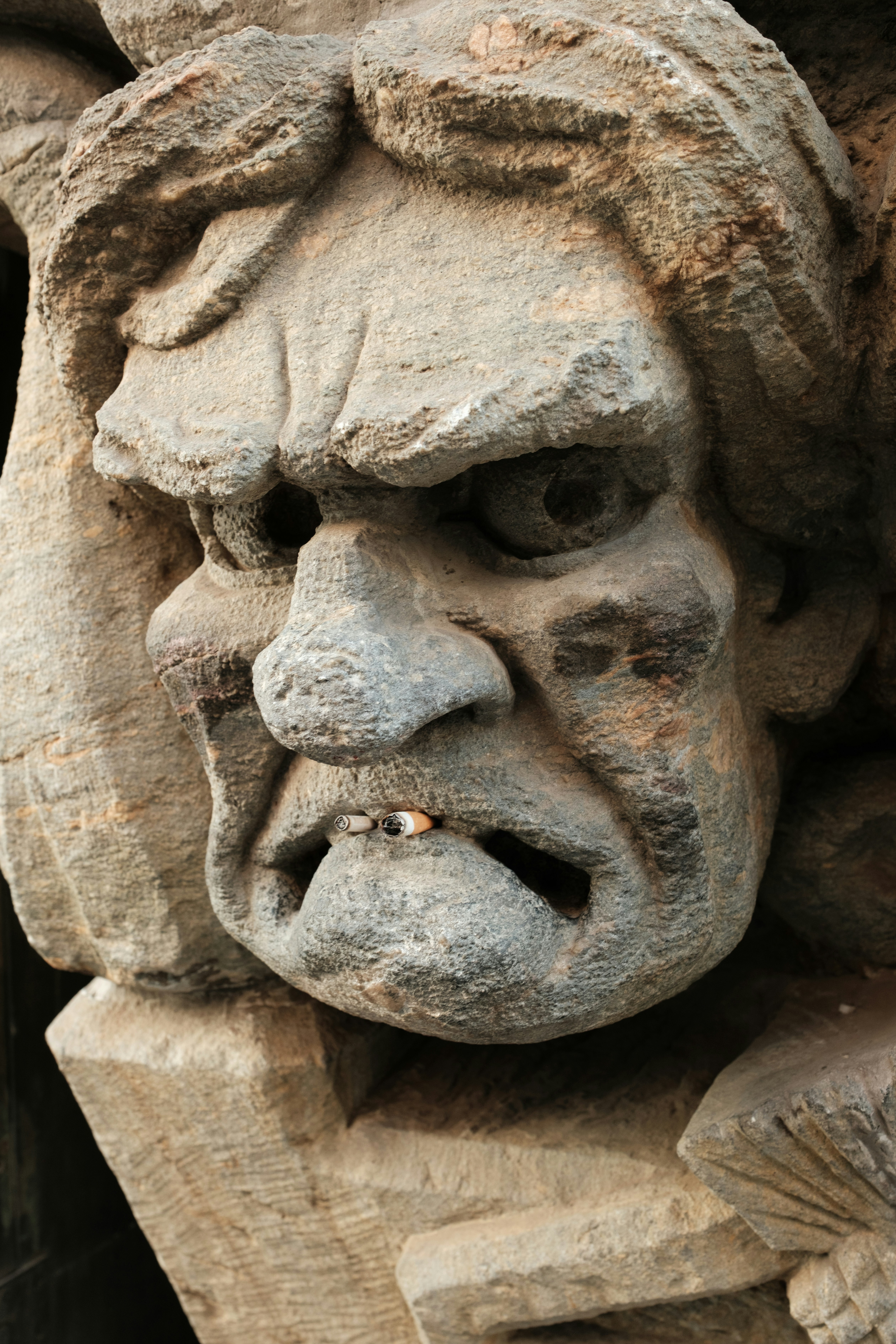 Talla en piedra de un rostro grotesco y enfadado con un cigarrillo.