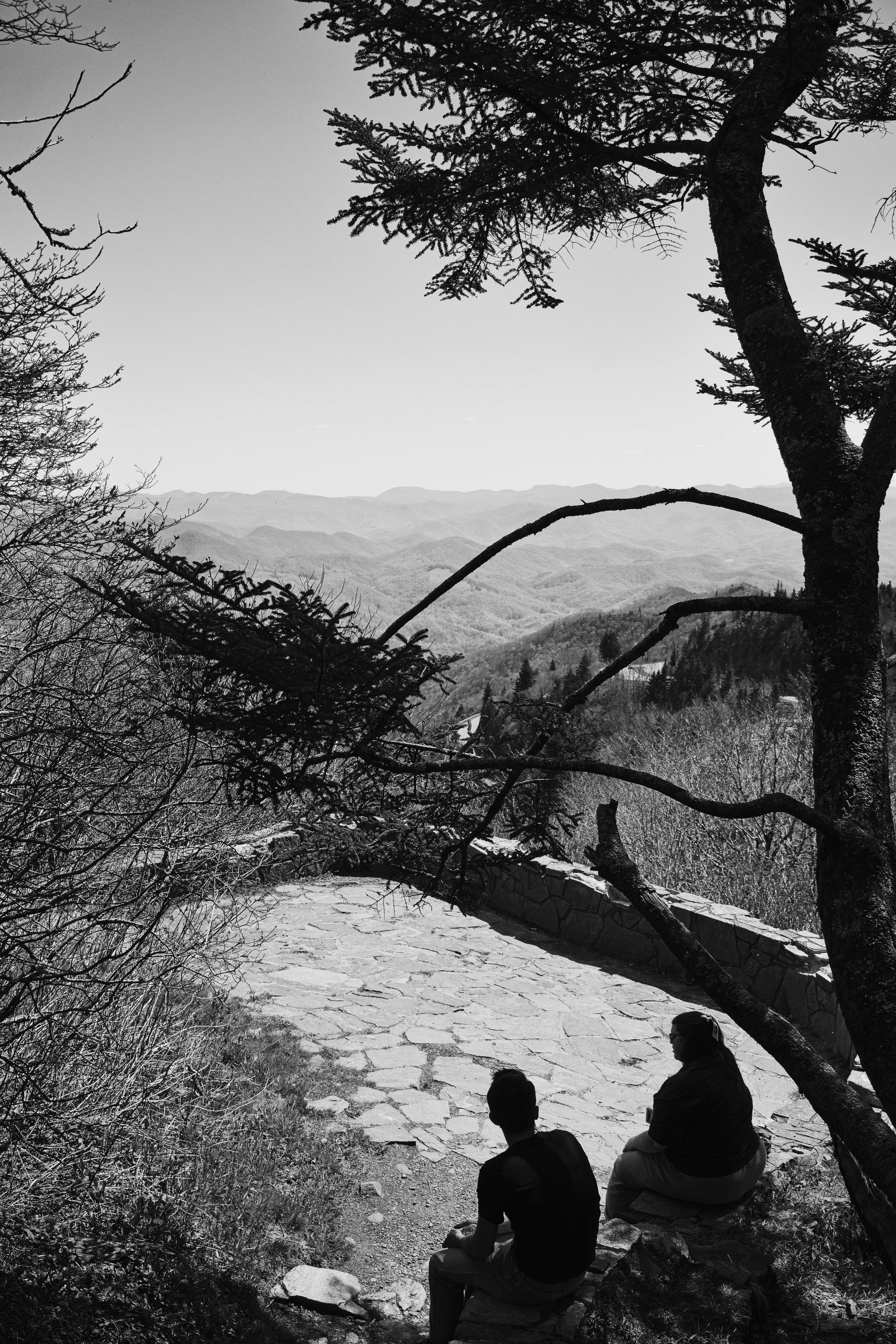 Due persone sono sedute su un affioramento roccioso che domina le montagne.