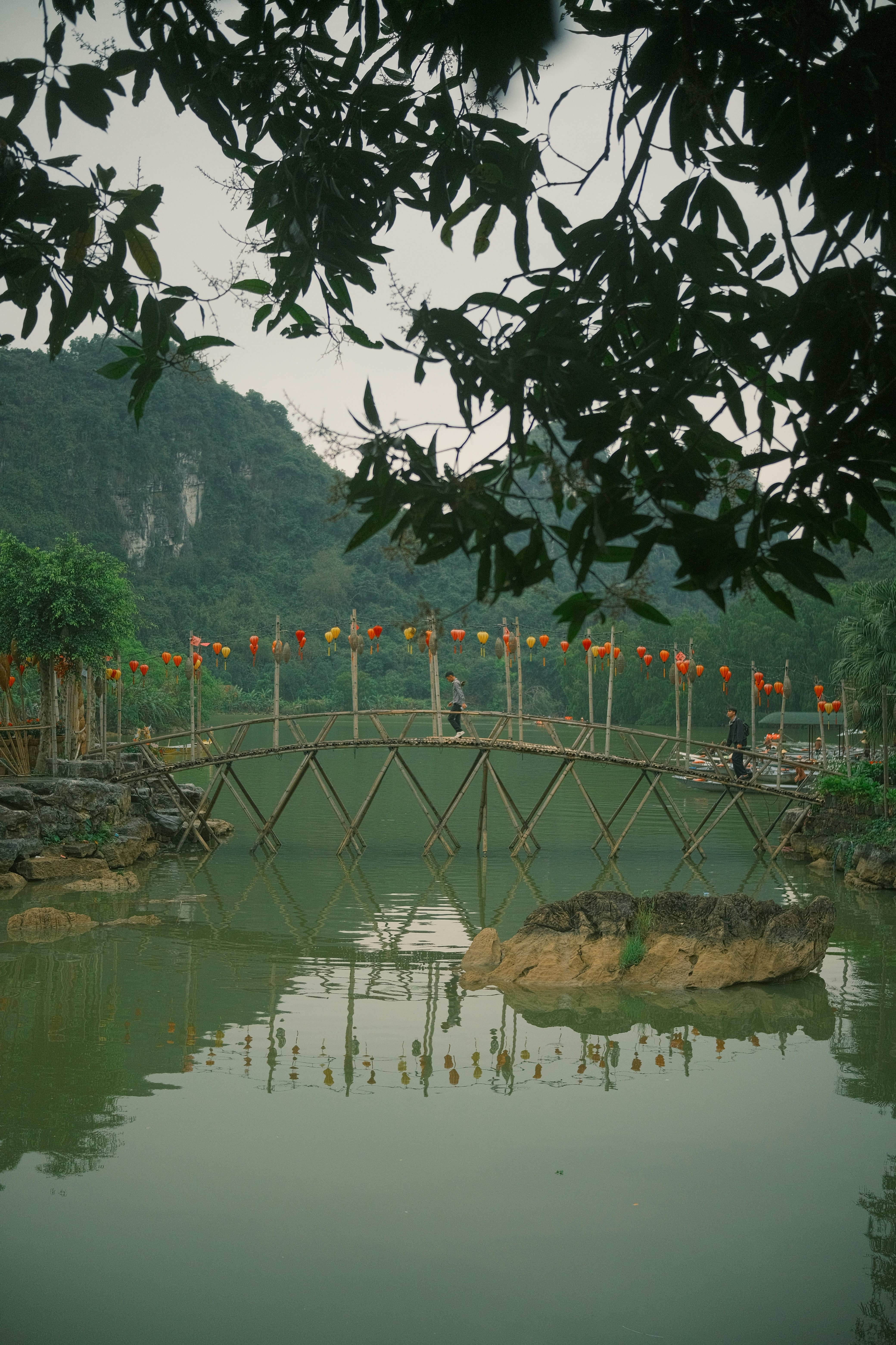 Ponte di bambù sull'acqua con lanterne e montagne.