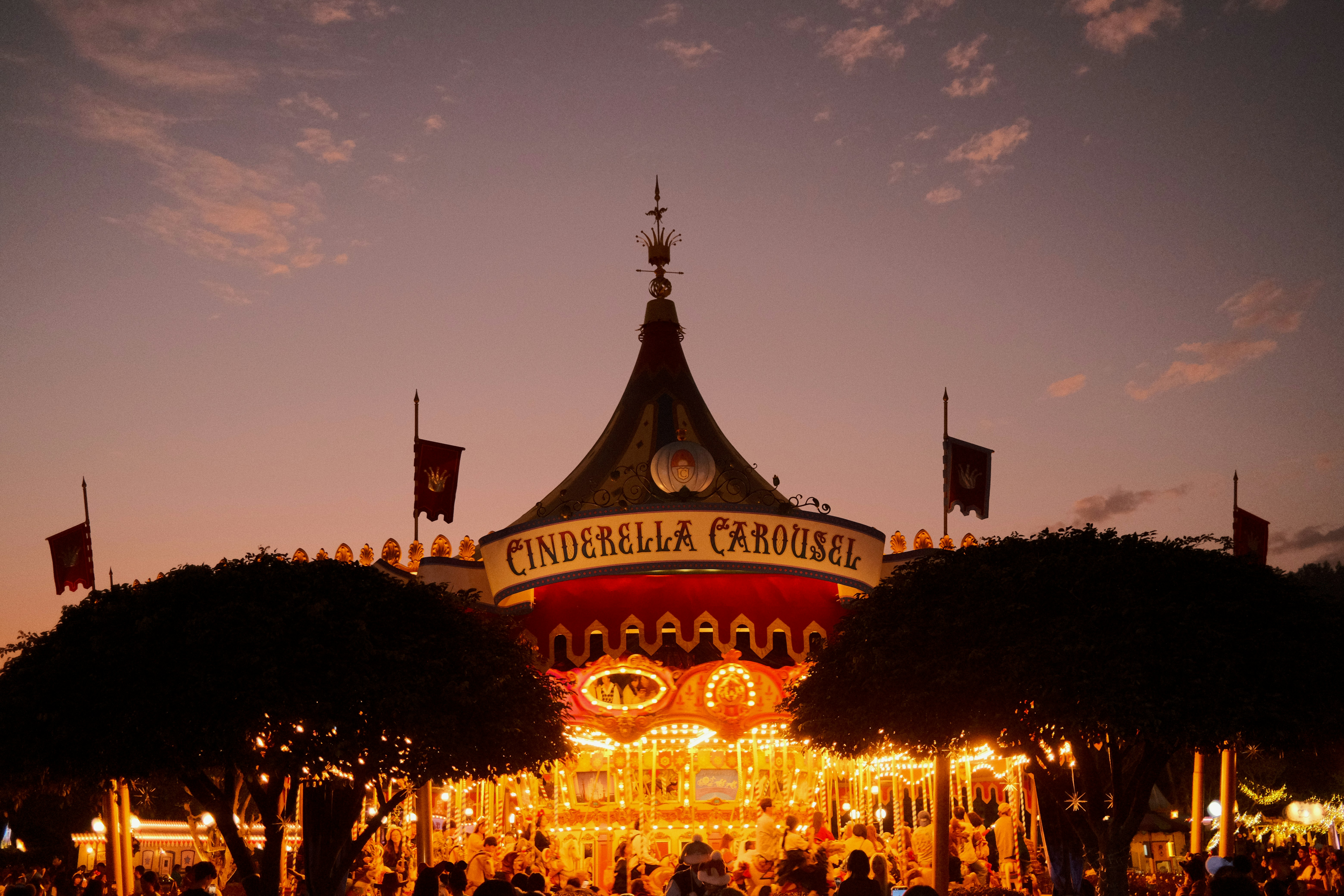 Cinderella carousel illuminated at dusk with silhouetted trees.