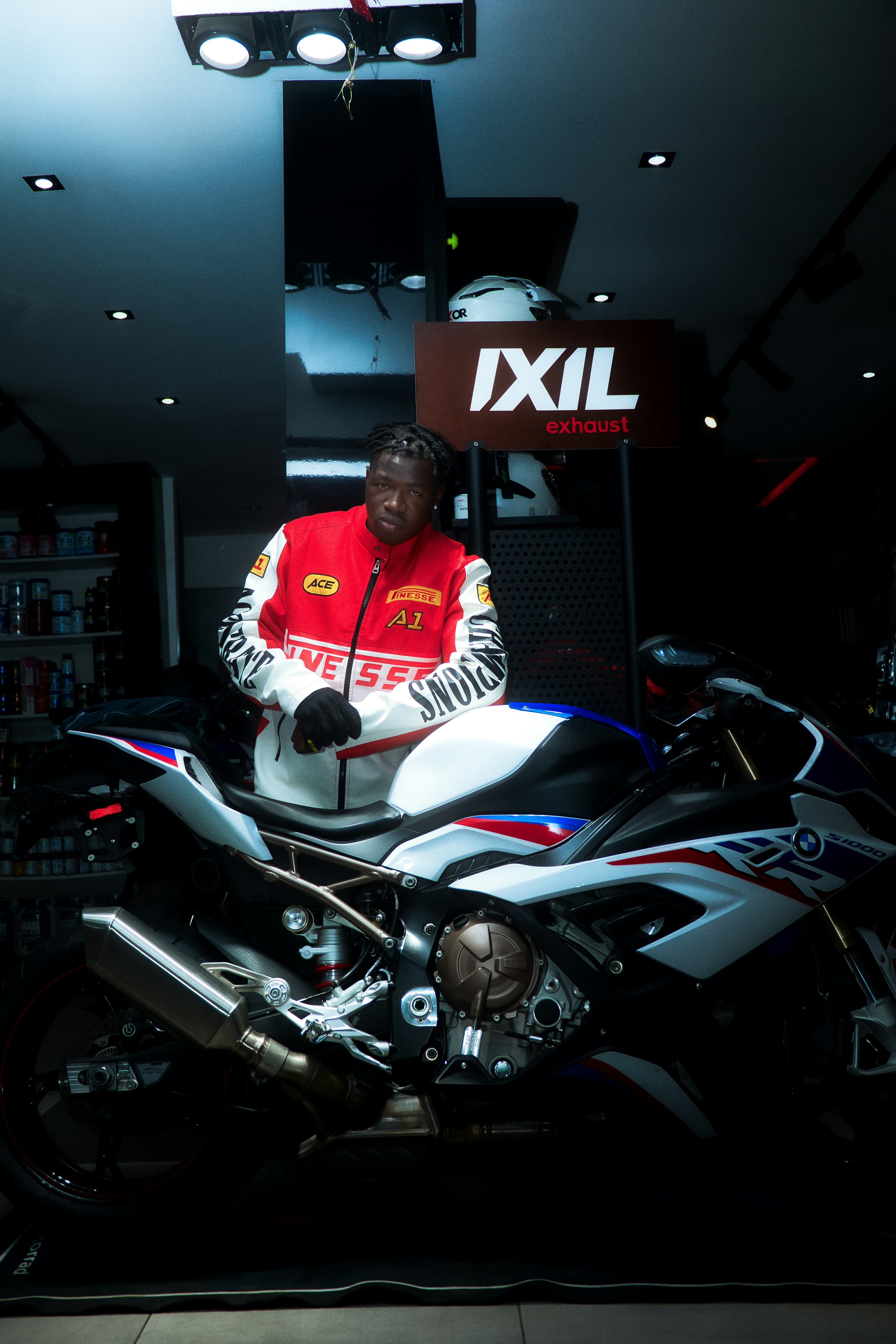 A man in a red jacket stands by a motorcycle.