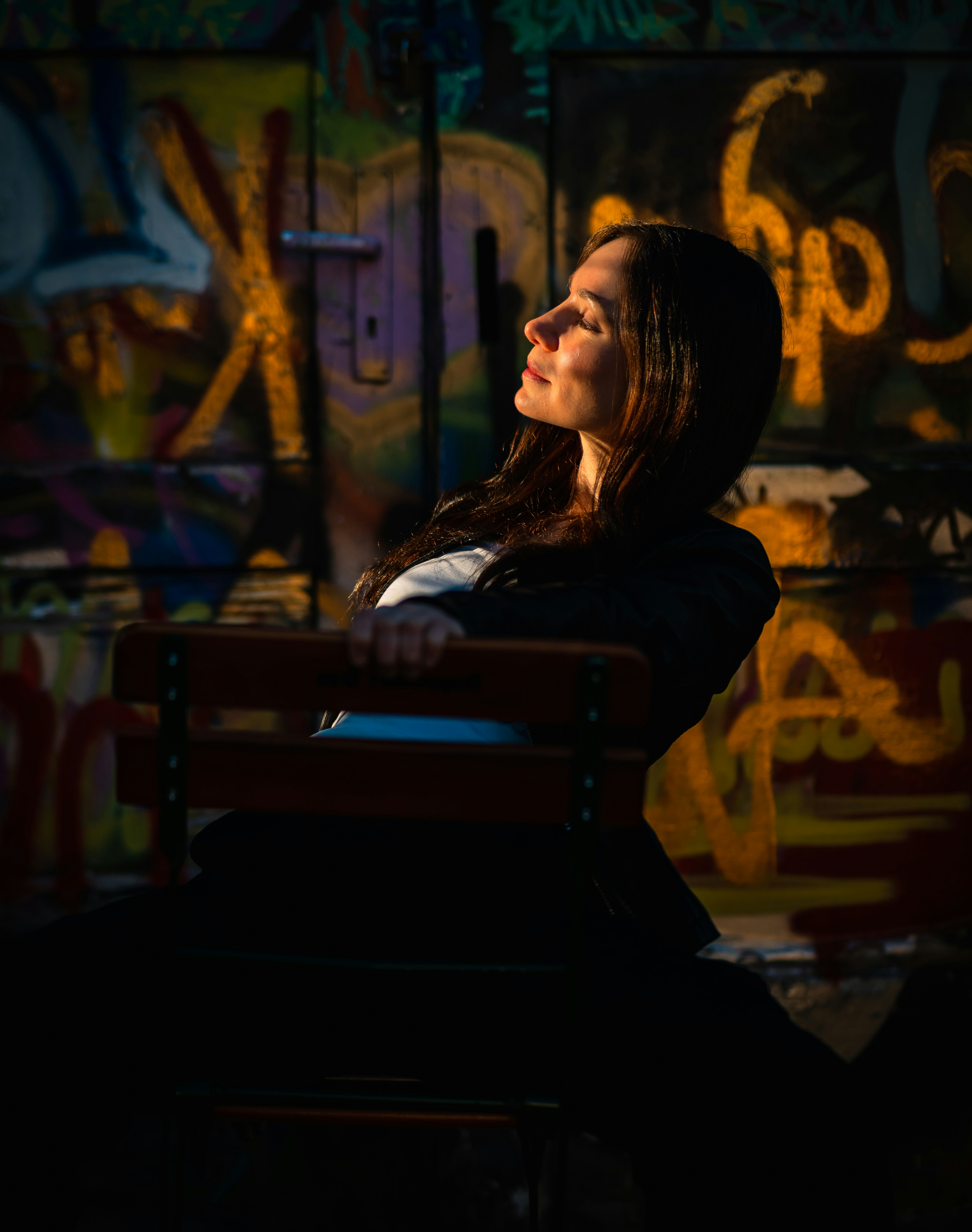 Woman sitting in front of graffiti wall in sunlight