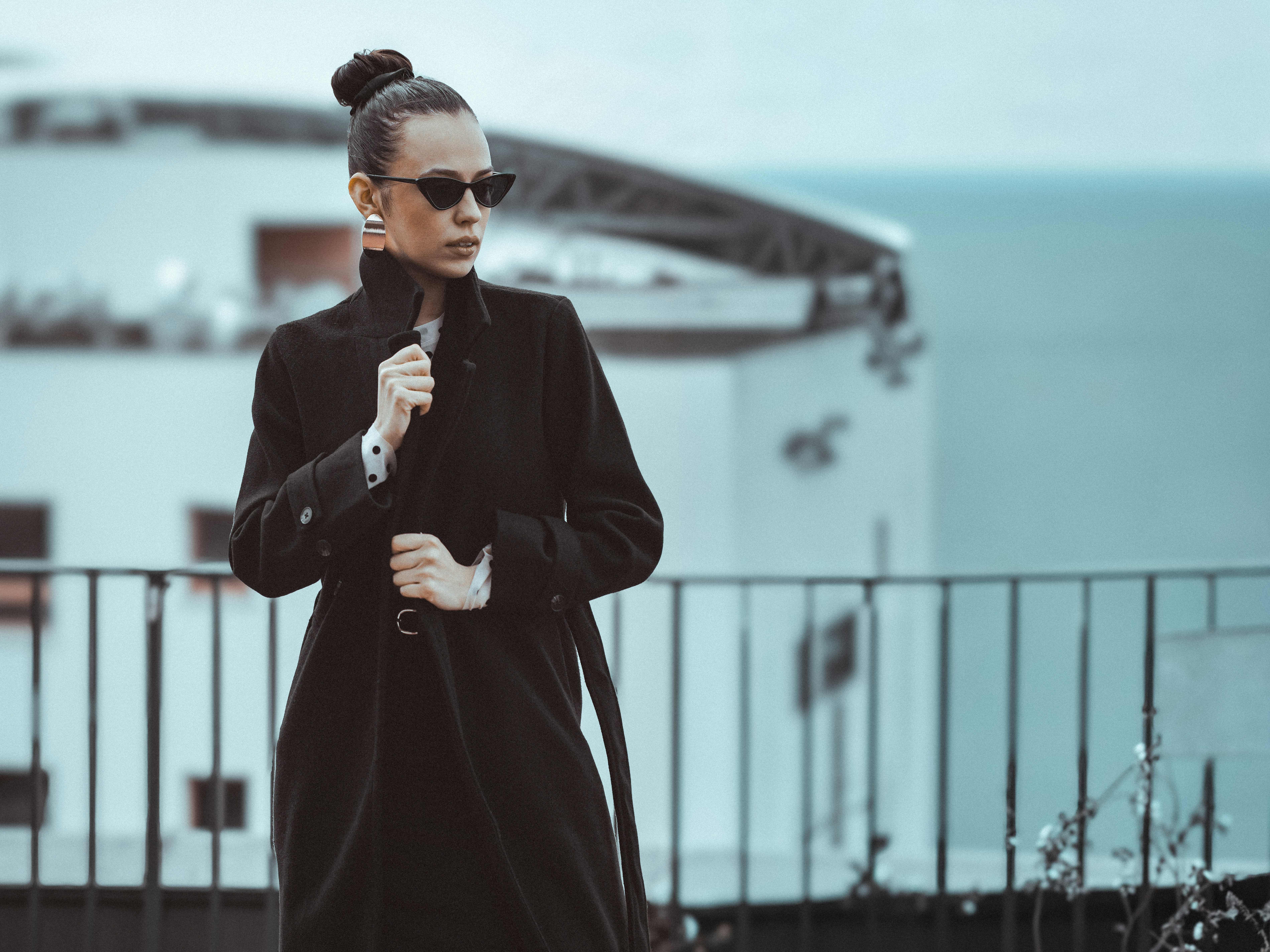 Frau im schwarzen Mantel und Sonnenbrille draußen