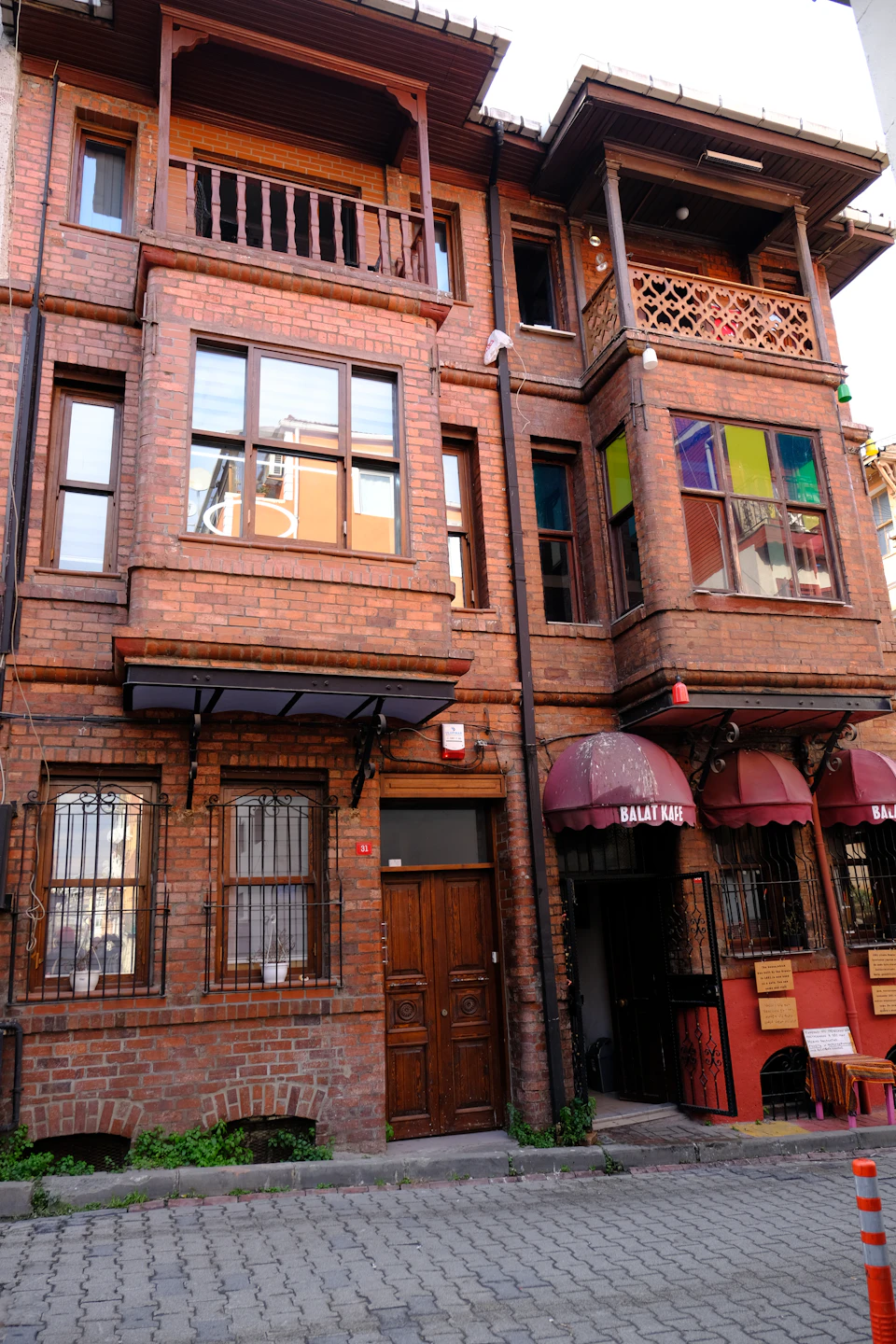 Two-story brick building with balcony and porch, both featuring red umbrellas on windows
