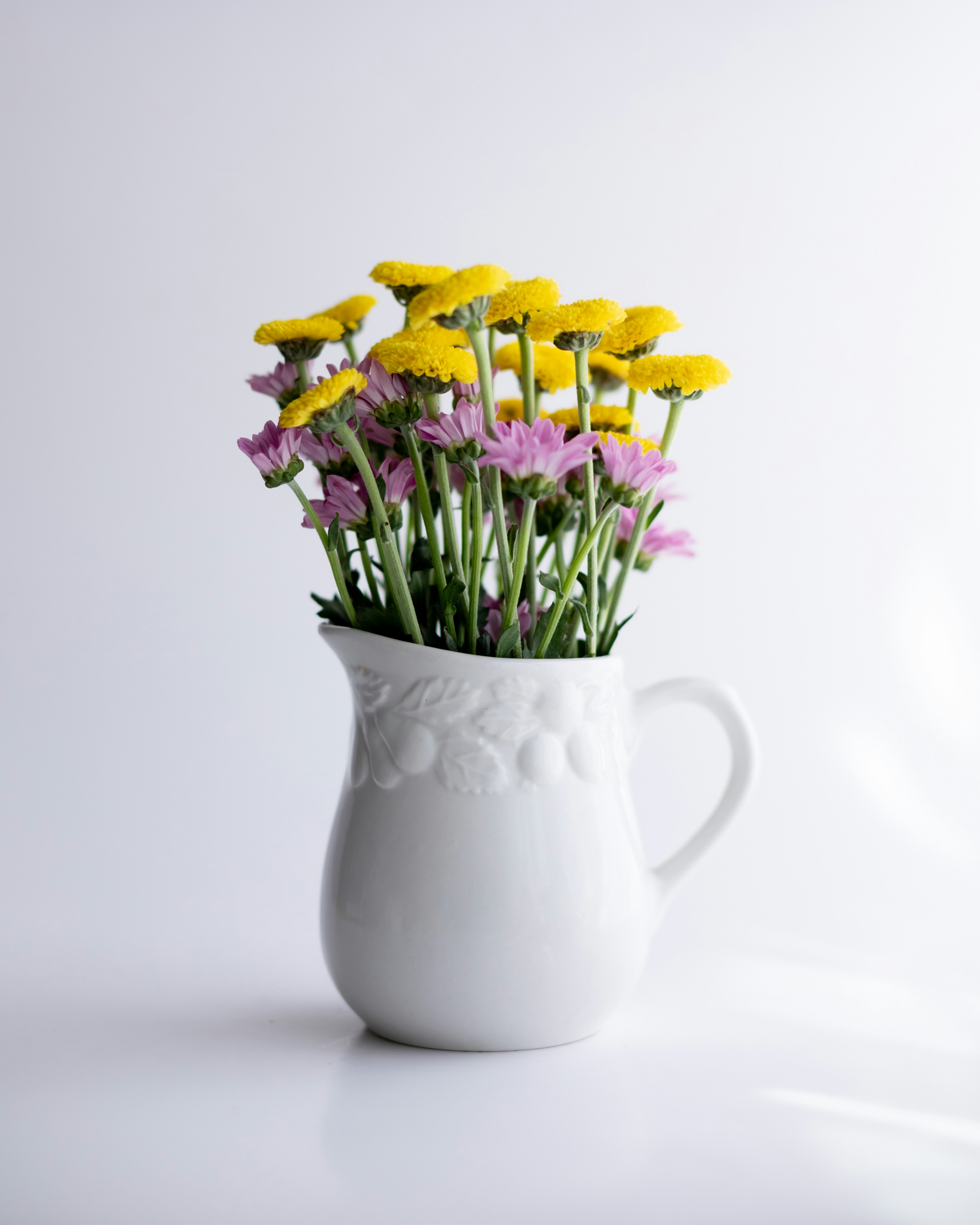 Yellow and purple flowers in a white pitcher.