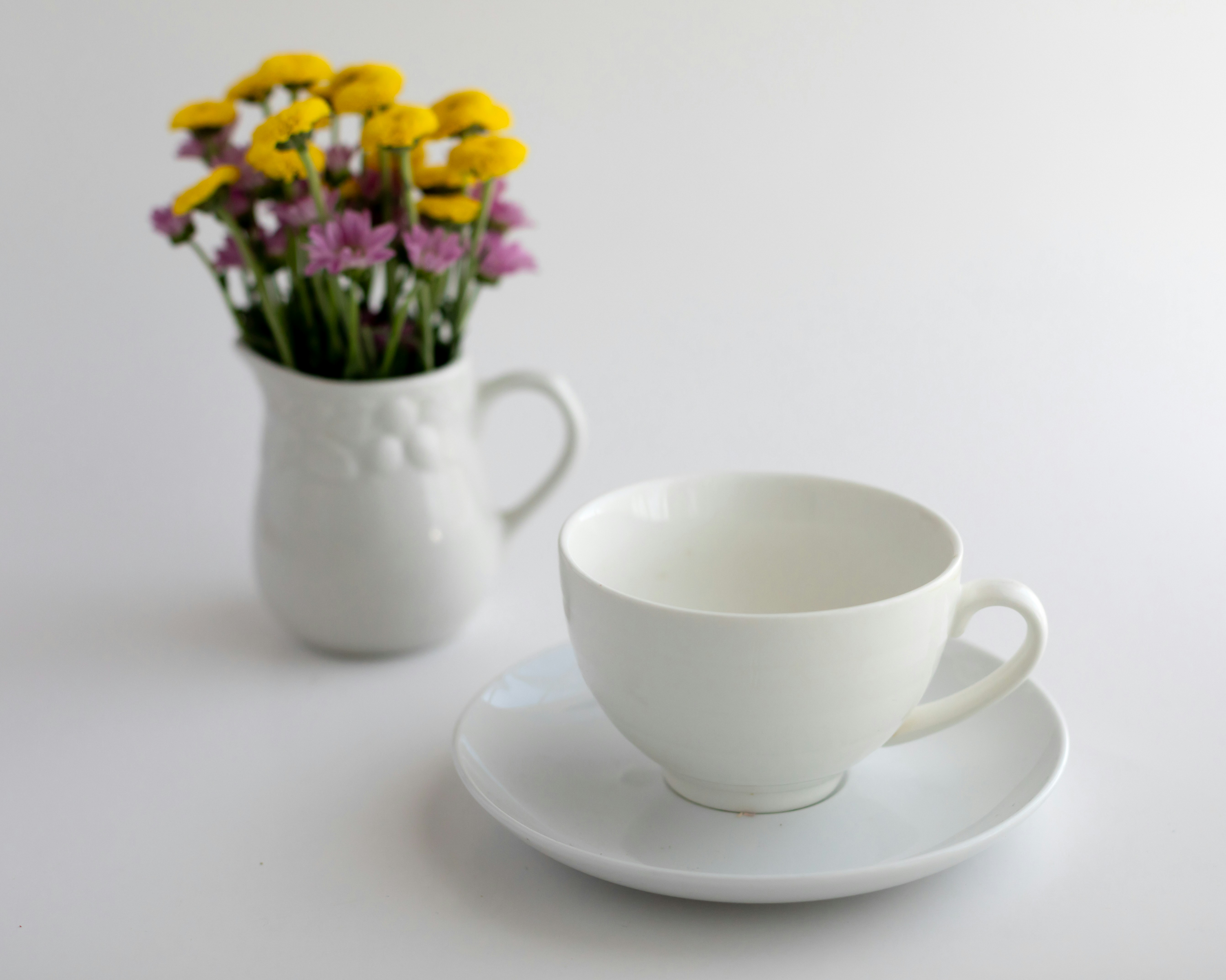 White teacup and saucer with flowers in pitcher