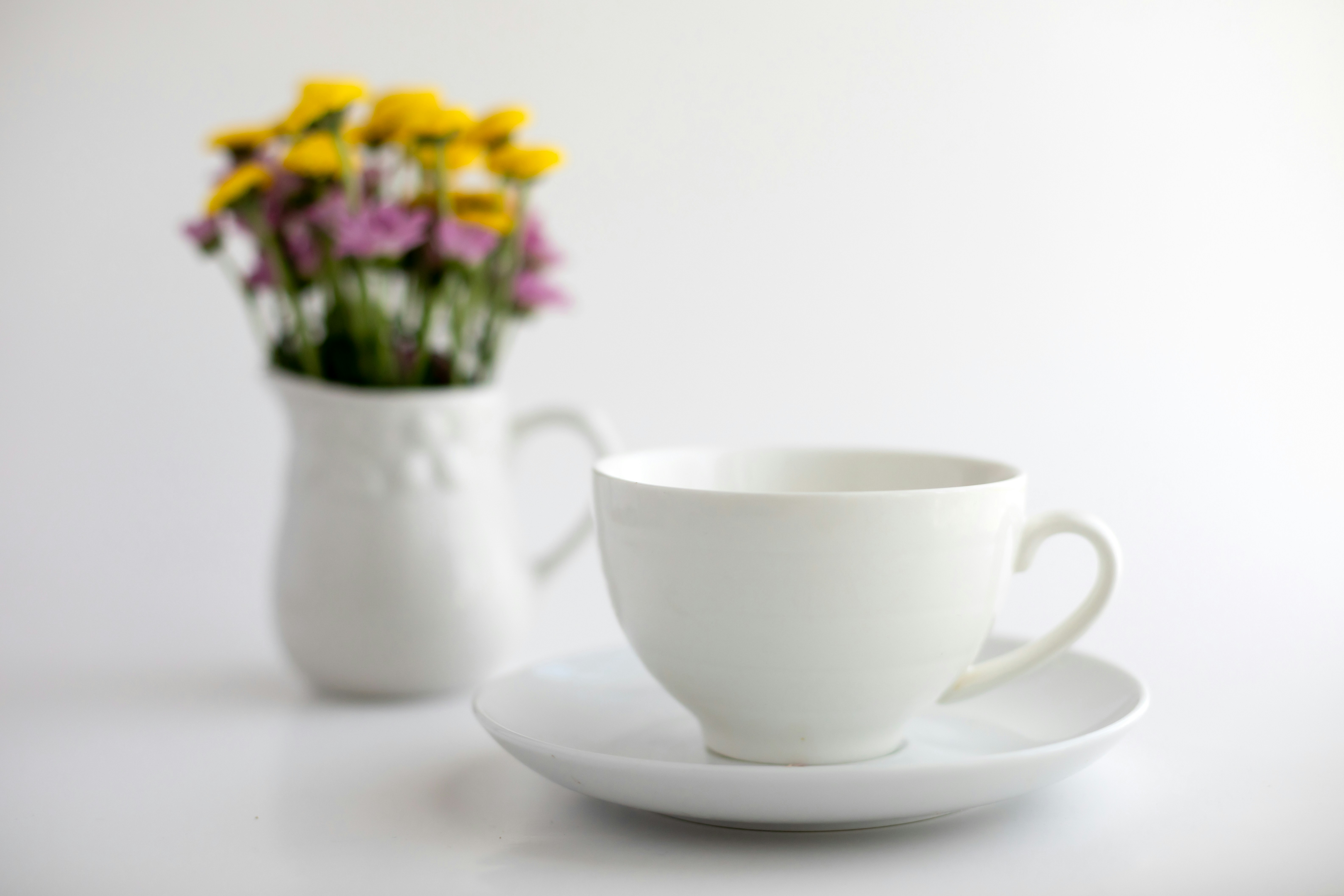 A white teacup and saucer with flowers in a vase.