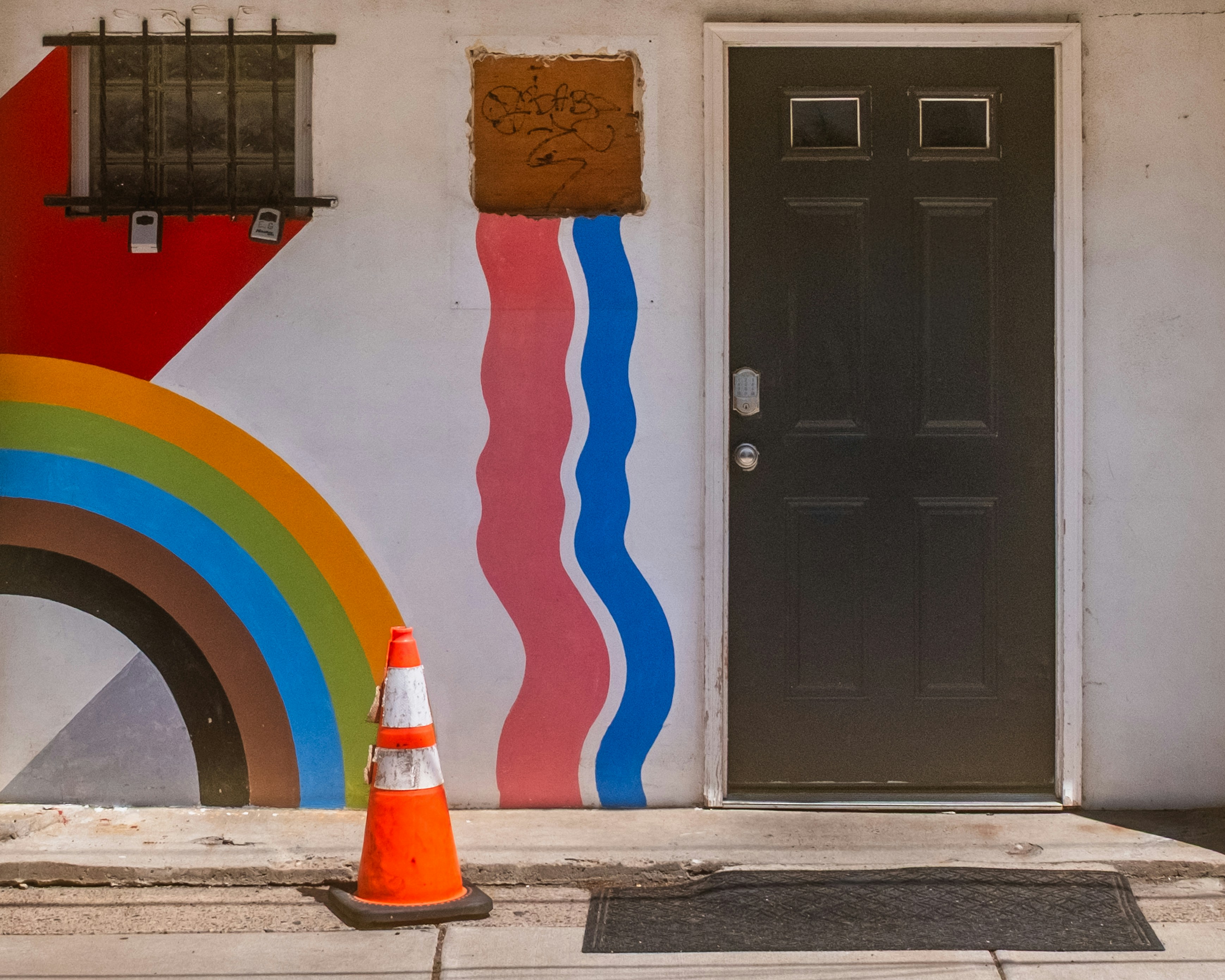 A black door with colorful mural and traffic cone.