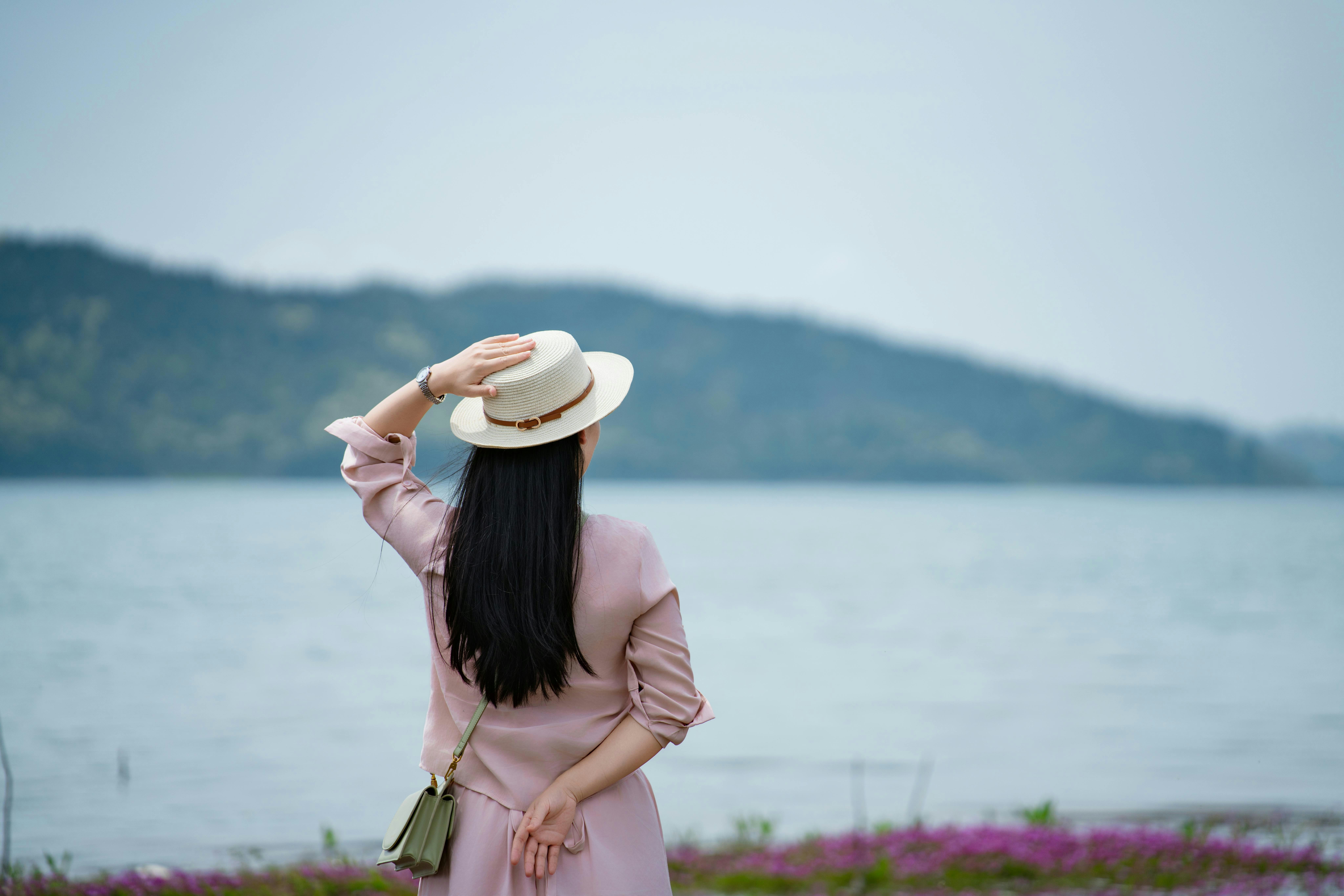 Woman in hat looking at a serene lake landscape.