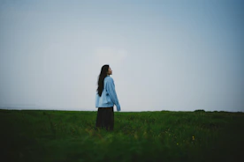 A woman stands in a grassy field looking up